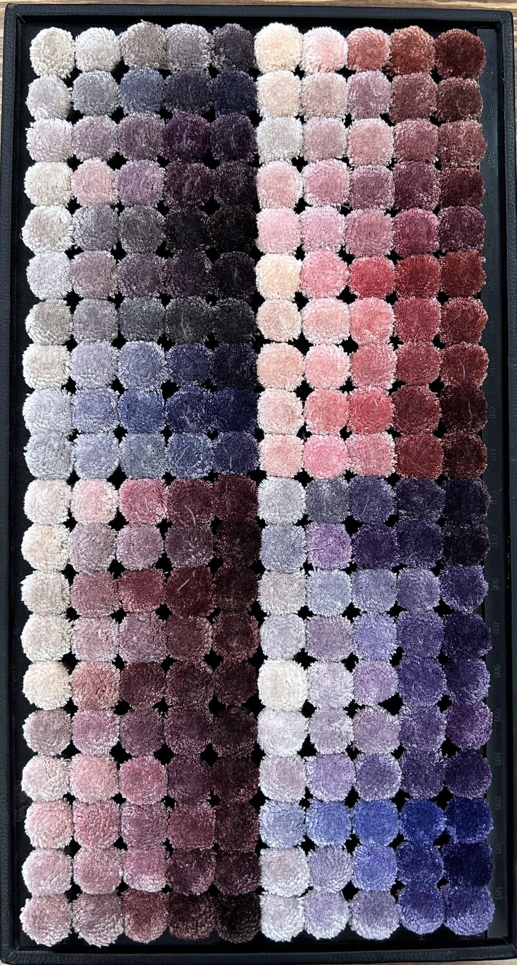 Close-up of a textile sample card with various colors of yarn tufts arranged in a grid pattern, featuring shades of gray, blue, pink, purple, and brown.
