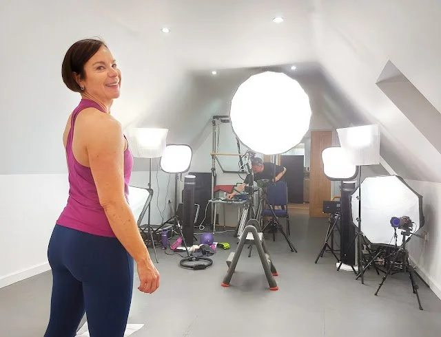 Behind‑the‑scenes view of Loraine in a heat‑filled studio with seven filming lights for the Pilates 34 workout.