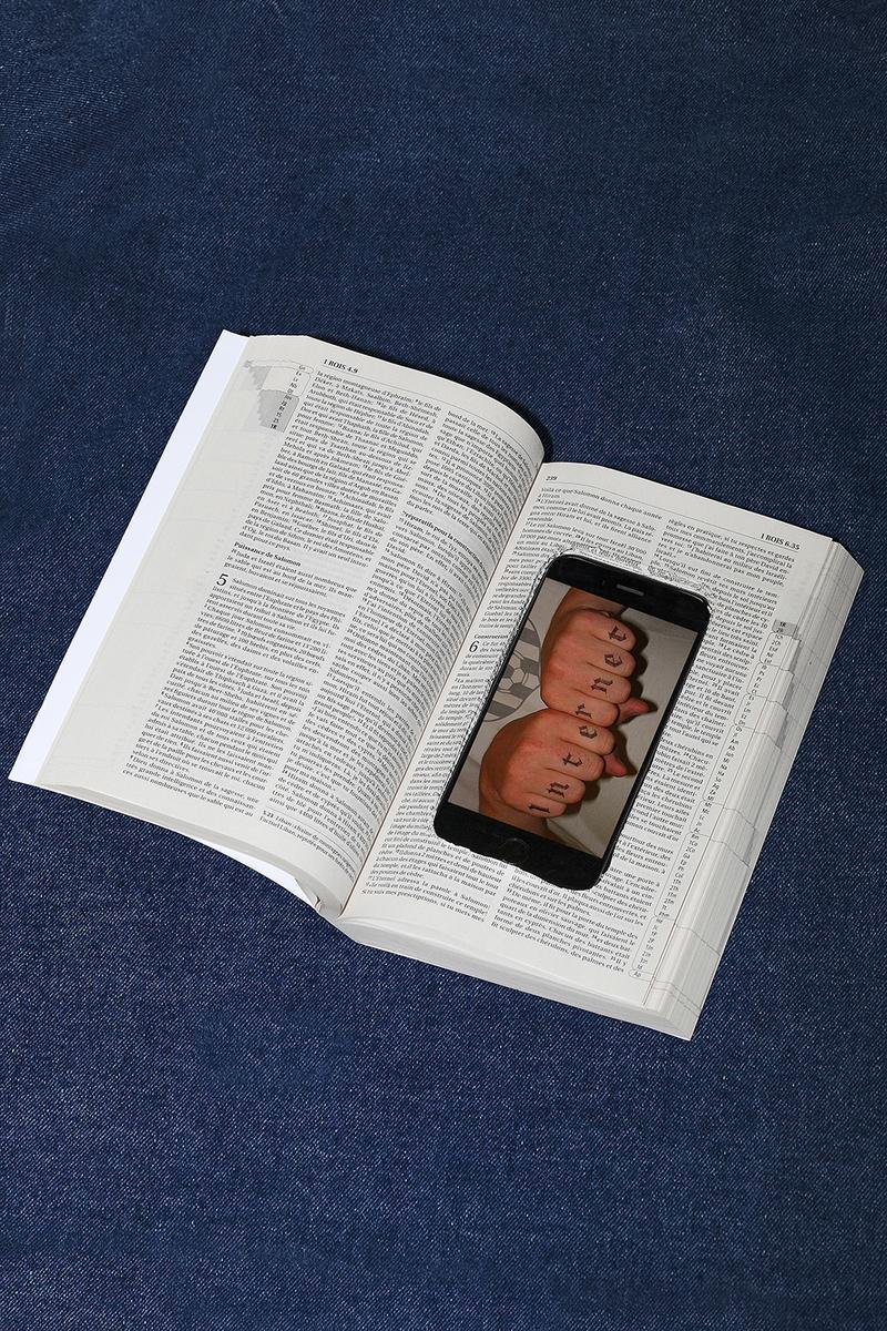Open book with a smartphone on top showing fingers with tattooed letters spelling 'together' on each finger.