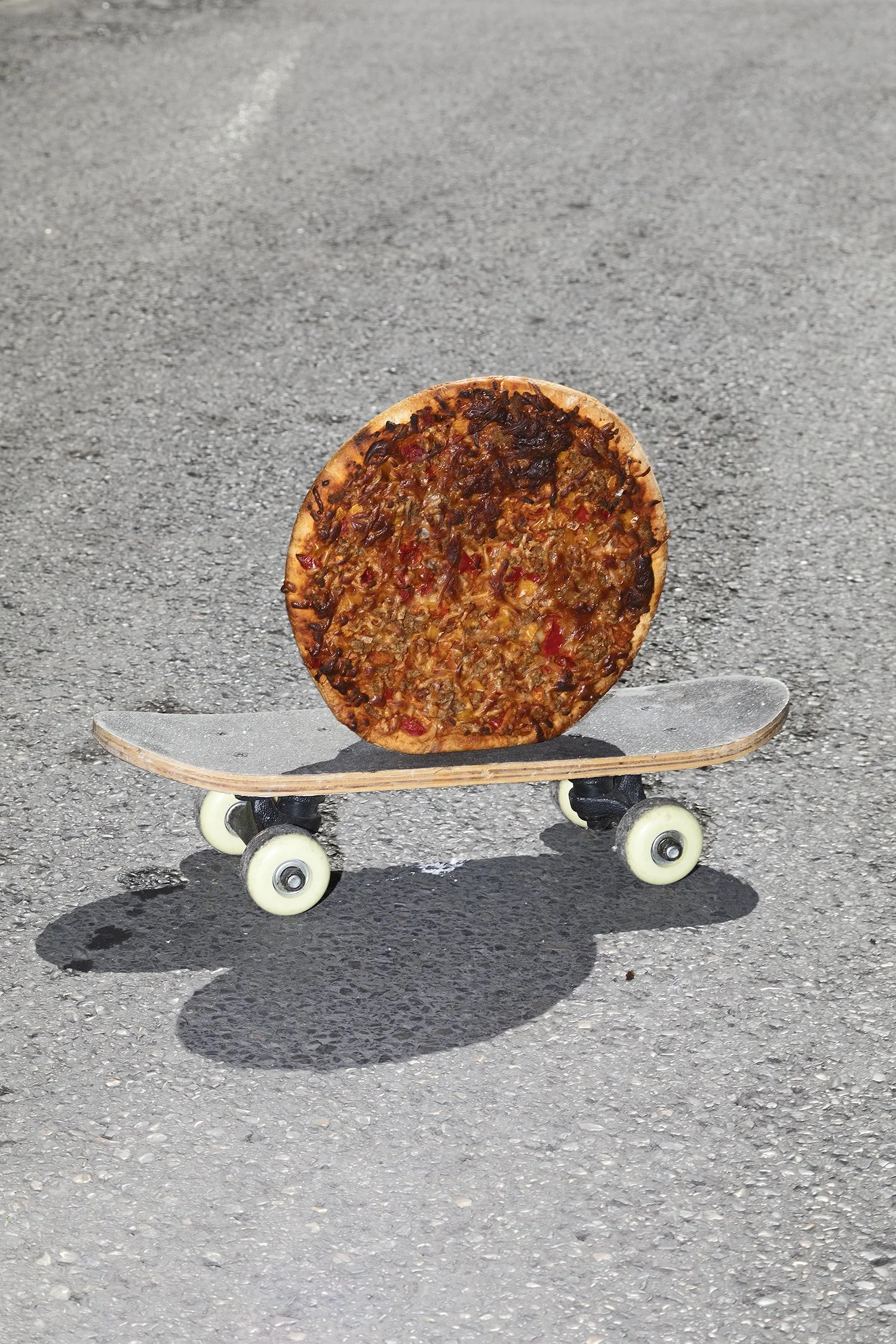 A pizza balanced on a skateboard on paved ground.