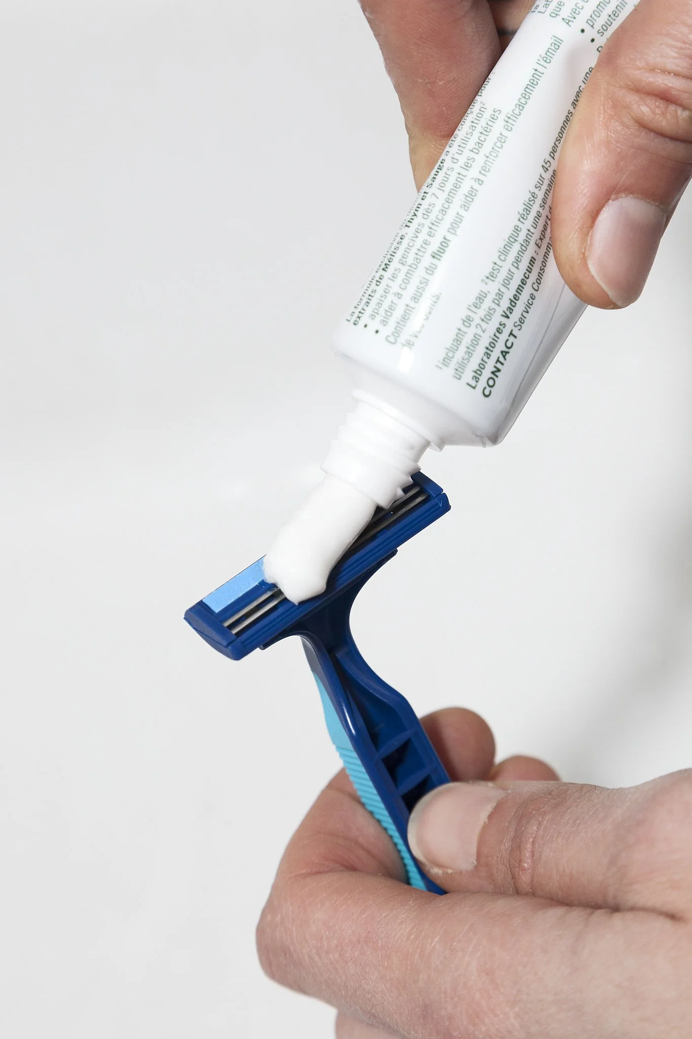 A person is applying shaving cream from a white tube onto a blue disposable razor.