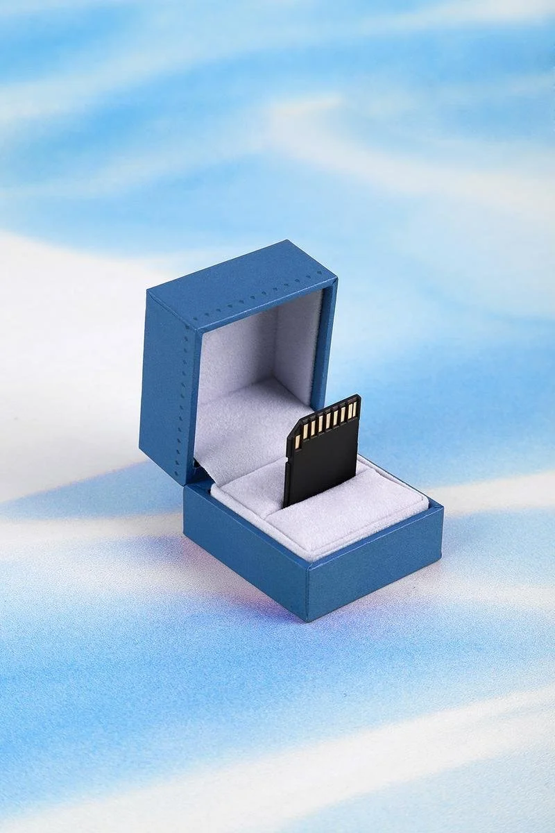 A blue jewelry box with a black microSD card inside, lined with white fabric.