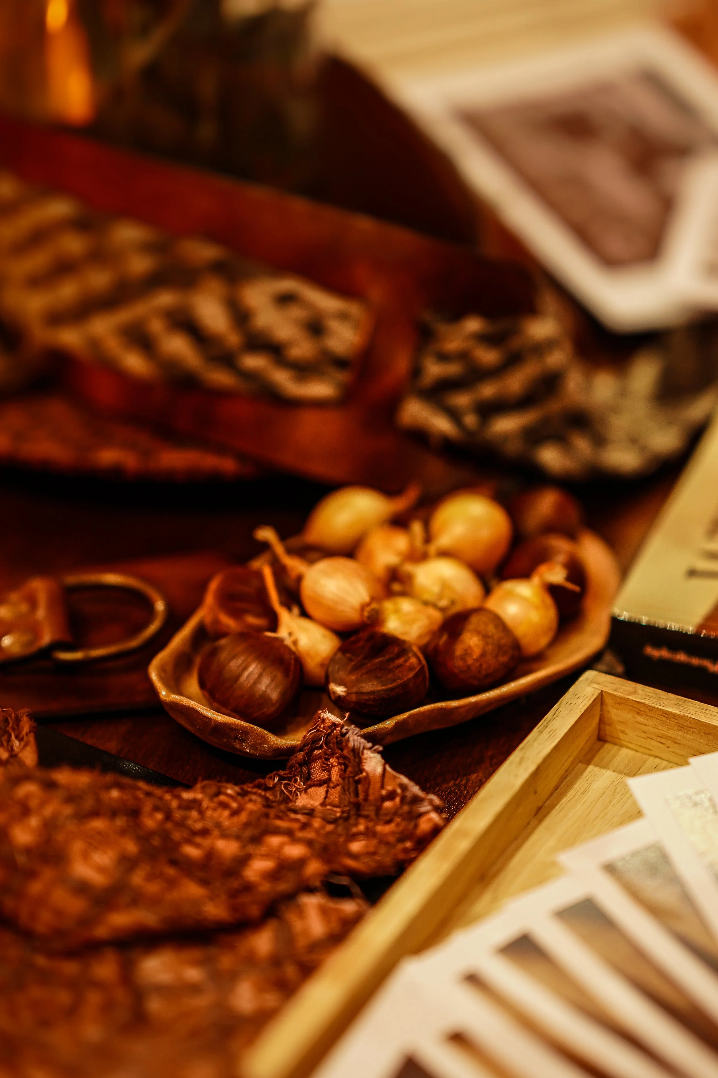 Close-up of a tray of assorted nuts, including hazelnuts and onions, on a wooden surface with a blurred background of food items.