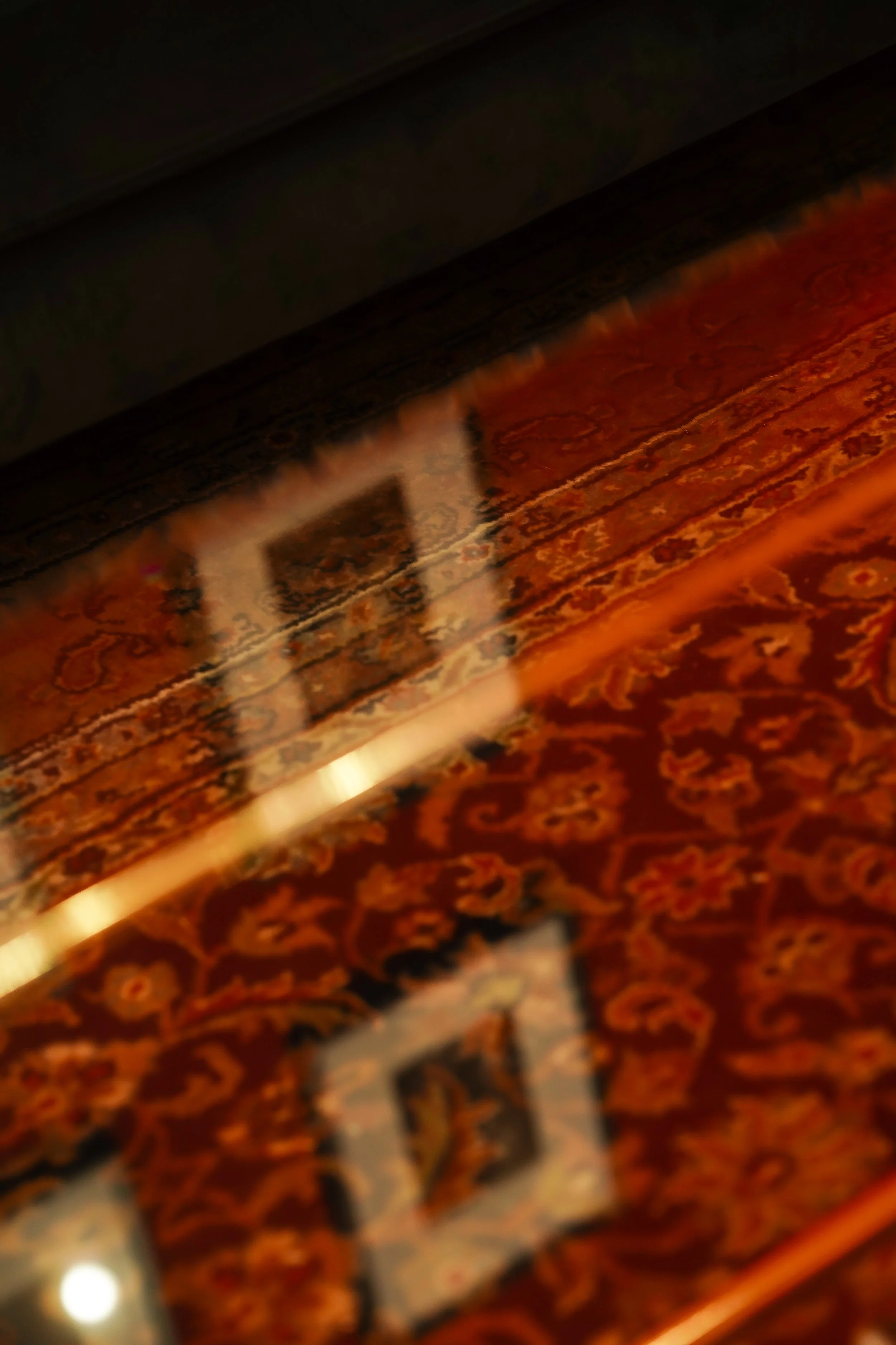 Close-up of an intricately designed carpet with orange and brown patterns, featuring a glossy reflective surface.