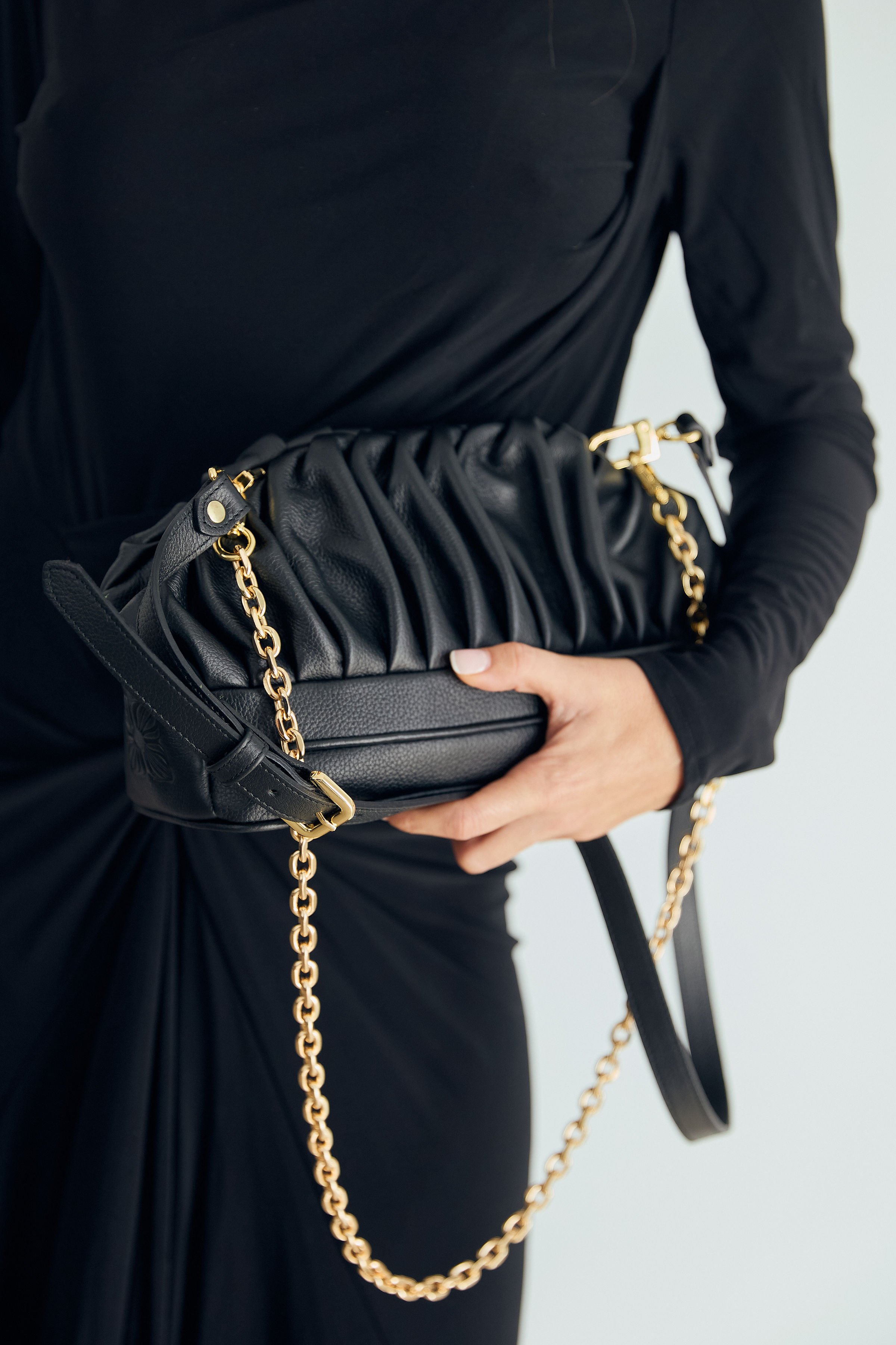 Person in black dress holding a black handbag with gold chain strap.