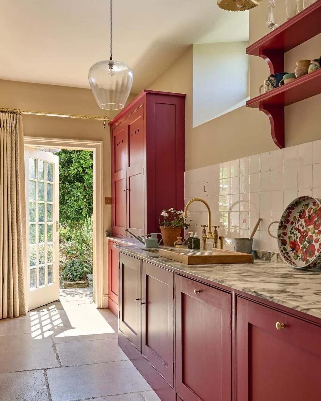 Our Cotswolds project butler's pantry leading out into the garden - with bespoke cabinetry painted in crimson red, Violetta marble worktops and traditional ceramic wall tiles. This beautiful old house is full of history, and we loved working with it 