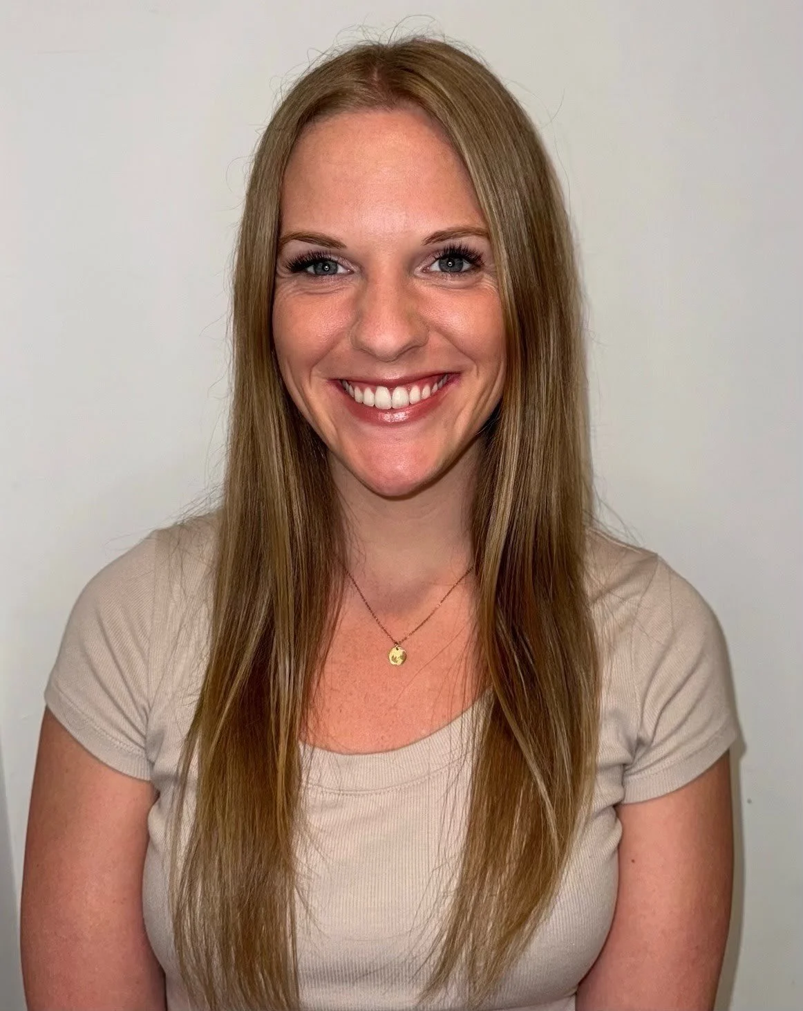 A young woman wearing a black graduation cap with a yellow tassel, smiling and holding a diploma outside a modern building with large glass windows.