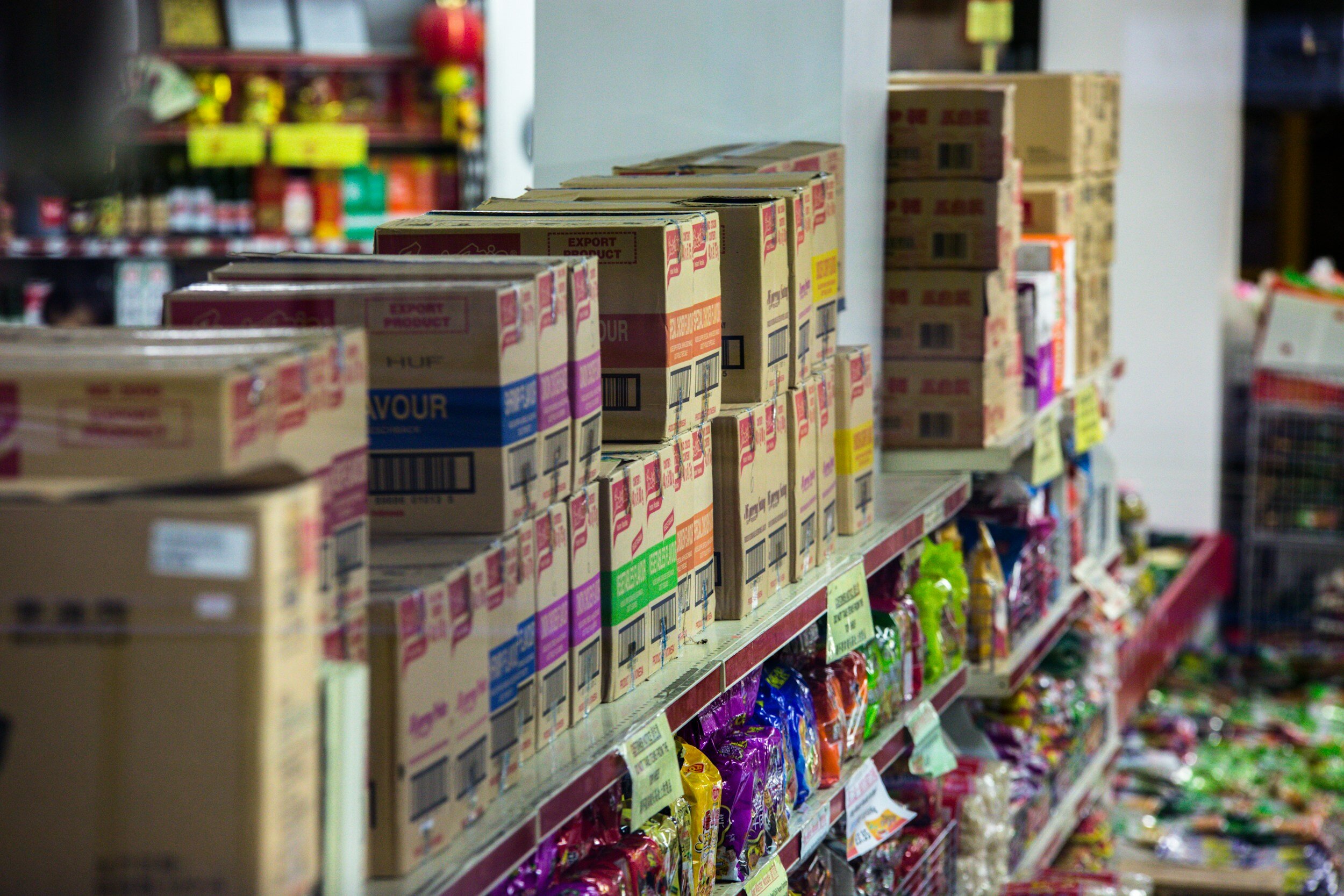 Shelves in a grocery store stocked with cardboard boxes, bags of snacks, and various products.