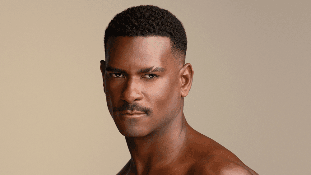 A shirtless man with short black hair and a serious expression looking at the camera against a plain background.