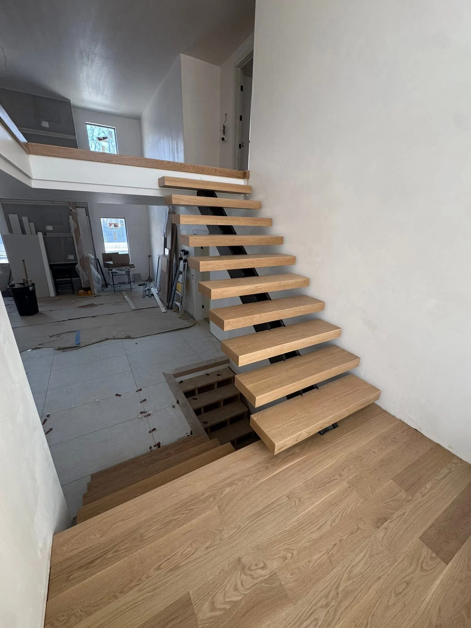 Angled view of a wooden staircase with open risers, leading to an upper floor, under construction in a house.