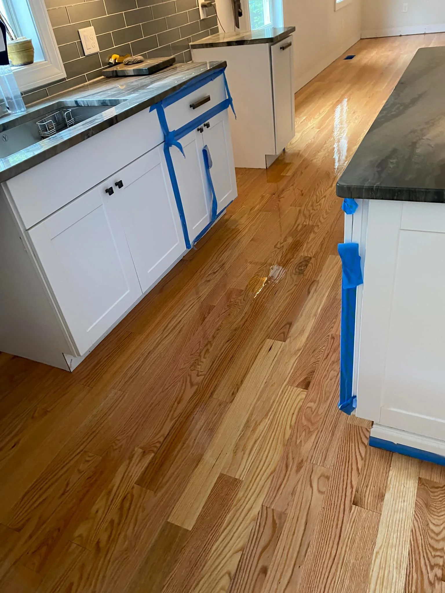 Kitchen with white cabinets, dark countertop, and a hardwood floor. Blue painter's tape is on the cabinets, indicating ongoing work or protection.
