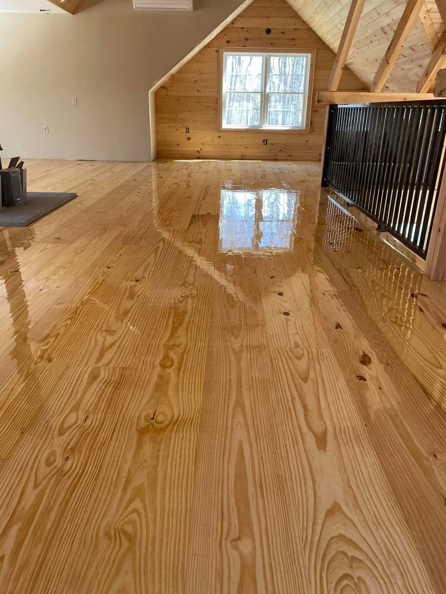Interior of a house with newly finished wooden floor, a wooden wall with a window, and a staircase with black railings.