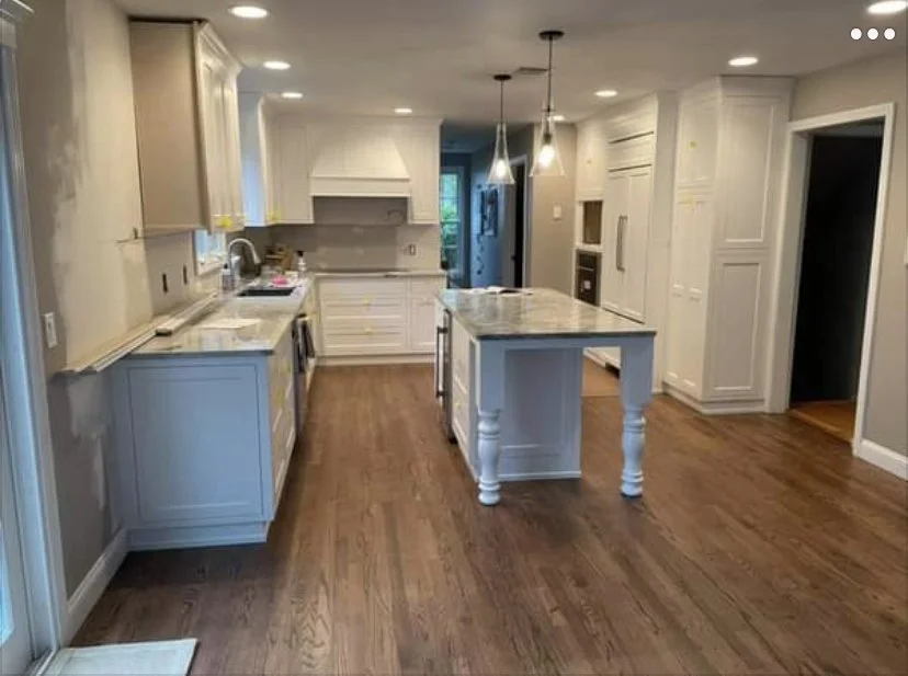 Spacious kitchen with white cabinets, a central island with a marble countertop, stainless steel appliances, hardwood floors, and hanging pendant lights.