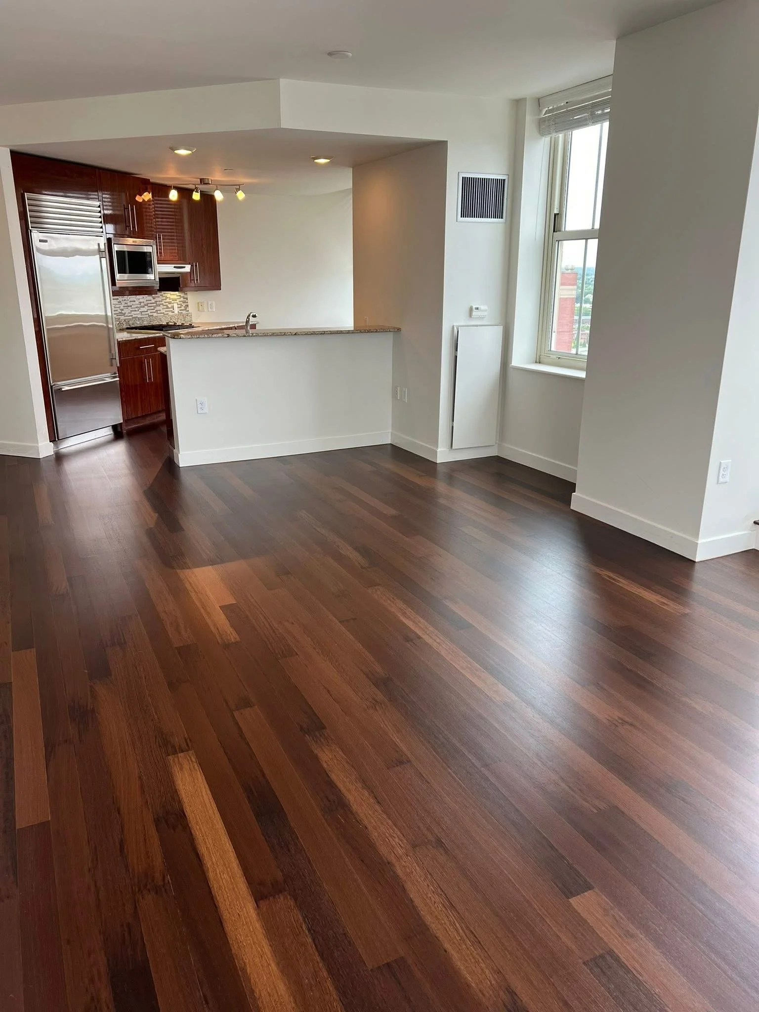 Open living room and kitchen area with hardwood floors, white walls, large window, and modern kitchen appliances.