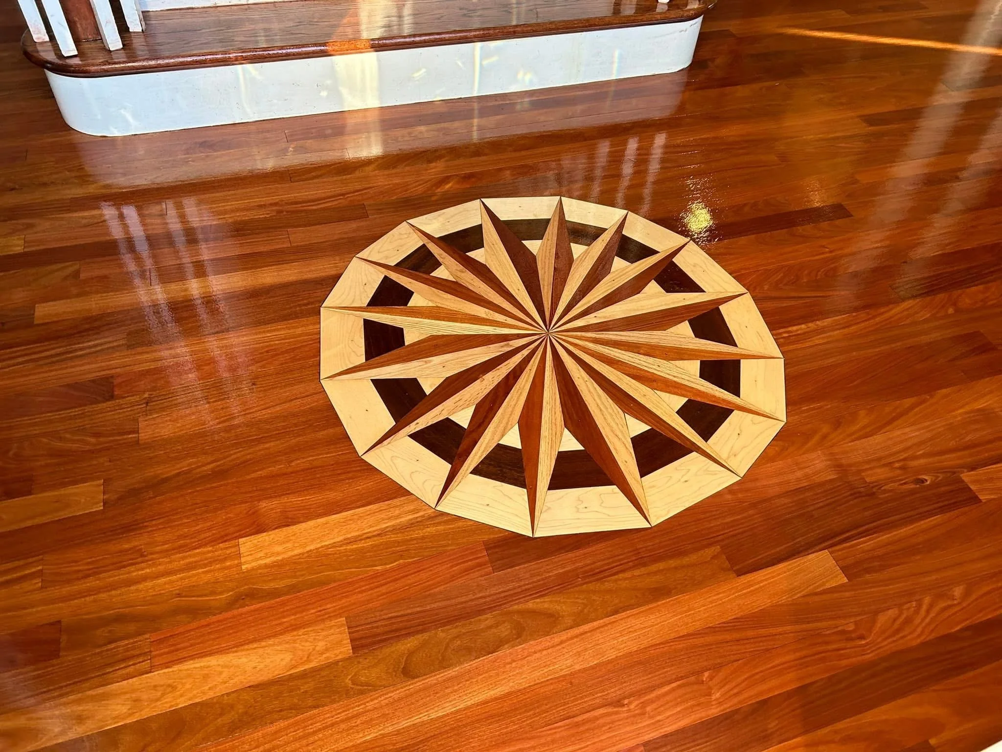 Decorative wooden floor medallion with starburst pattern on hardwood floor.