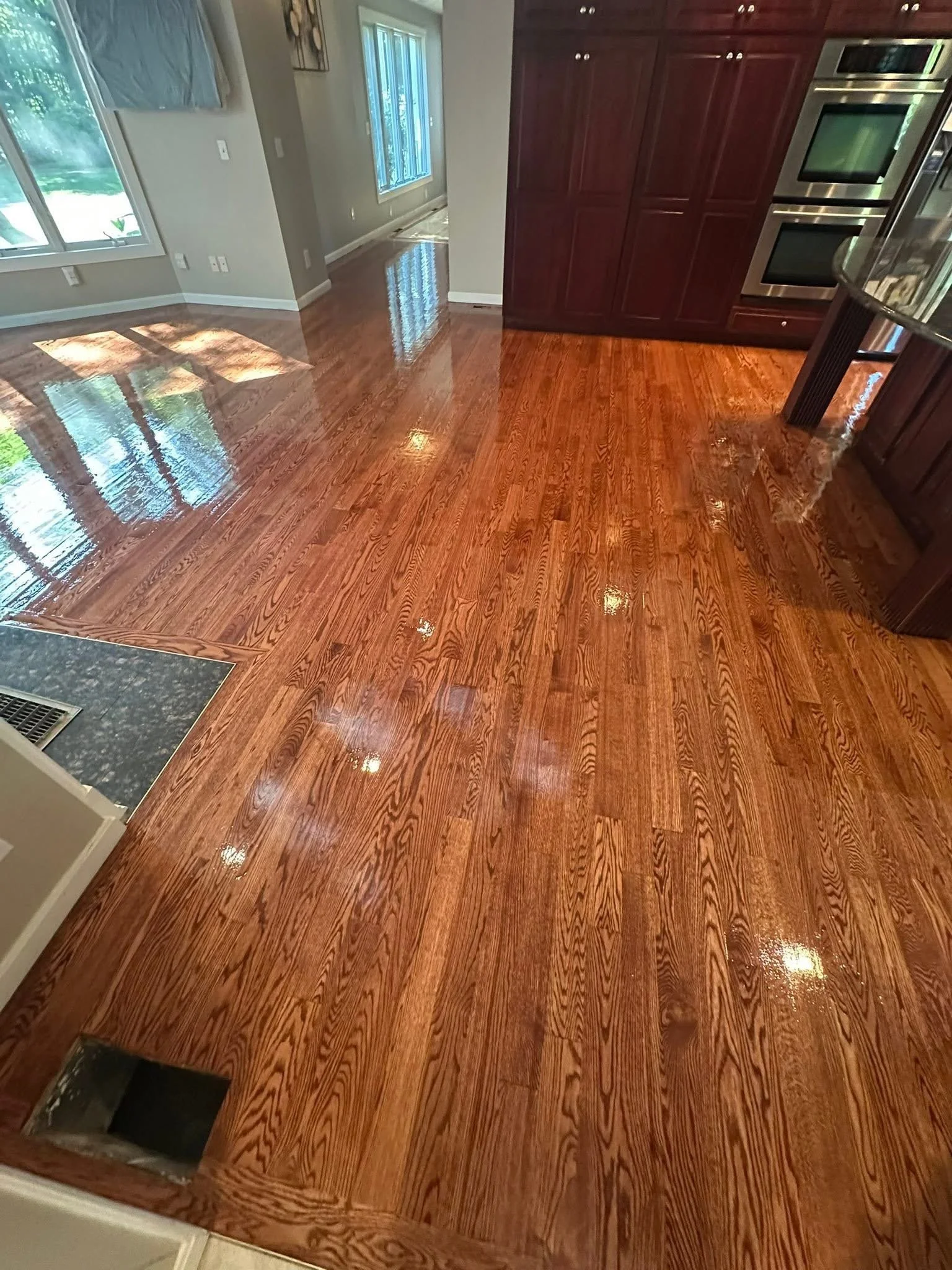 Shiny hardwood floor in a kitchen and dining area with sunlight coming through windows.