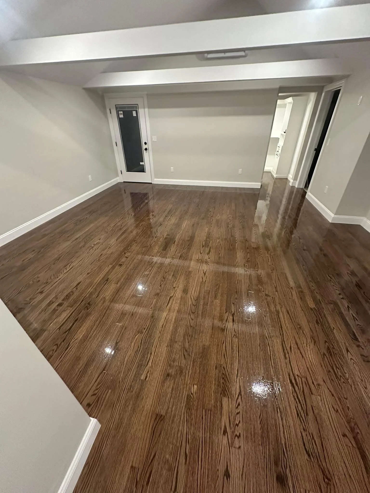 Empty room with polished wooden floors, white walls, and a doorway leading to another room.