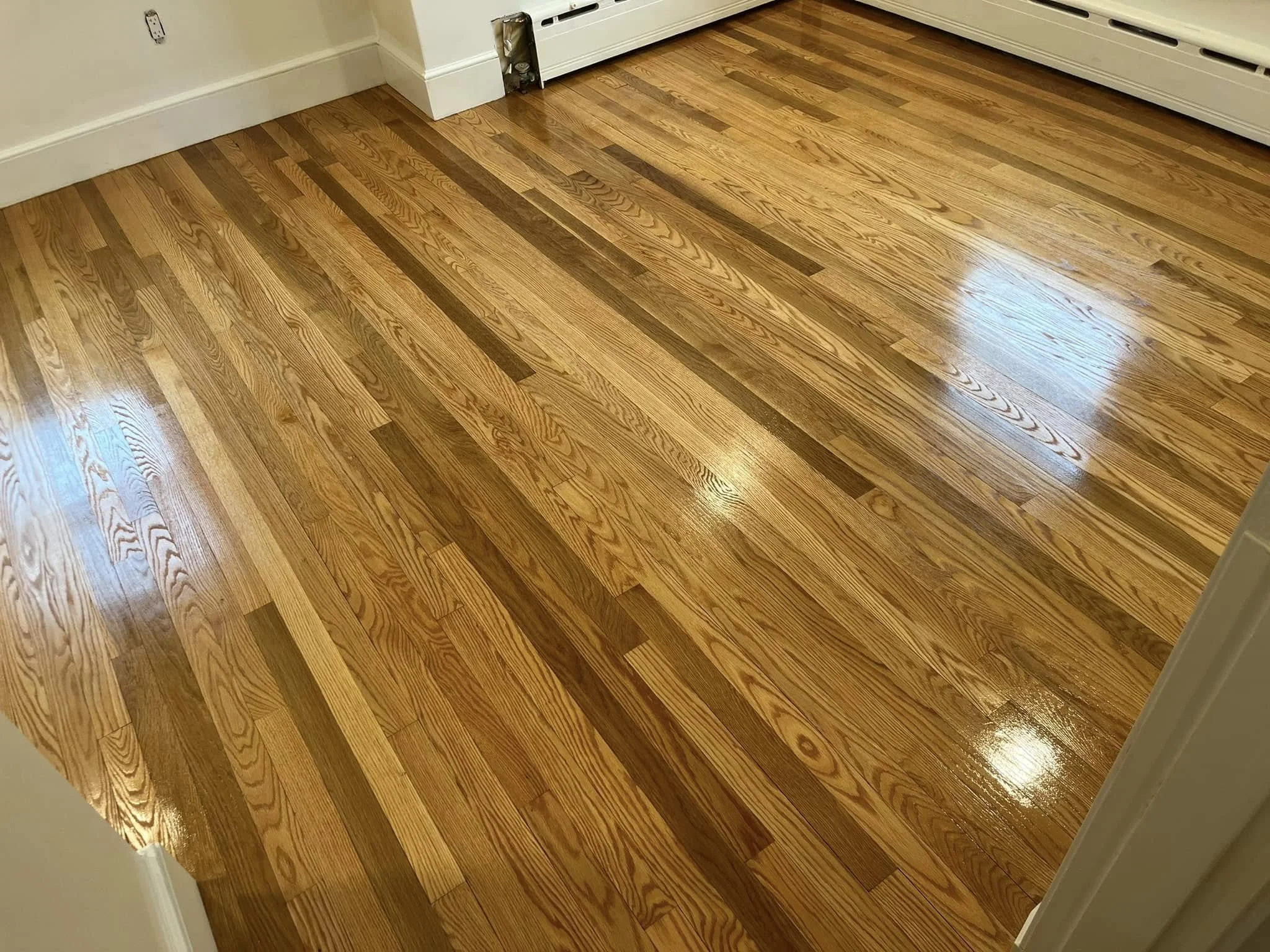 Clean, polished hardwood floor in a room with white baseboards and a radiator cover.