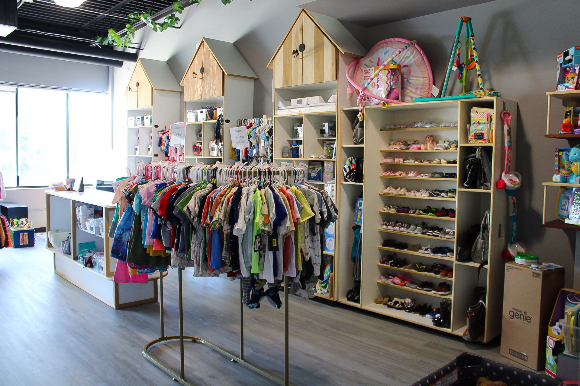 Children's thrift store with clothing racks and shelves filled with toys and shoes, bright natural light from windows.
