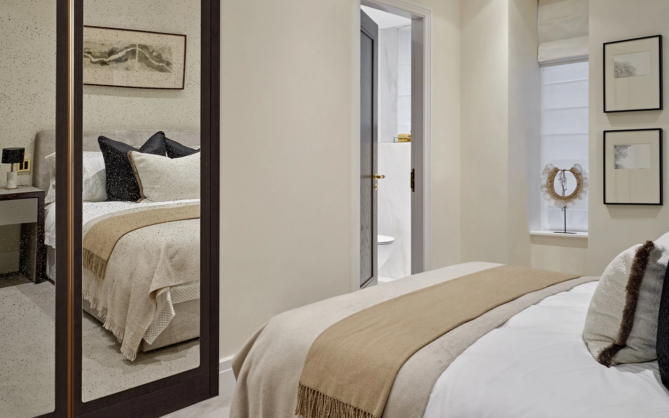 Bedroom with a grey velvet headboard, black and cream cushions and framed art in a Hyde Park apartment.