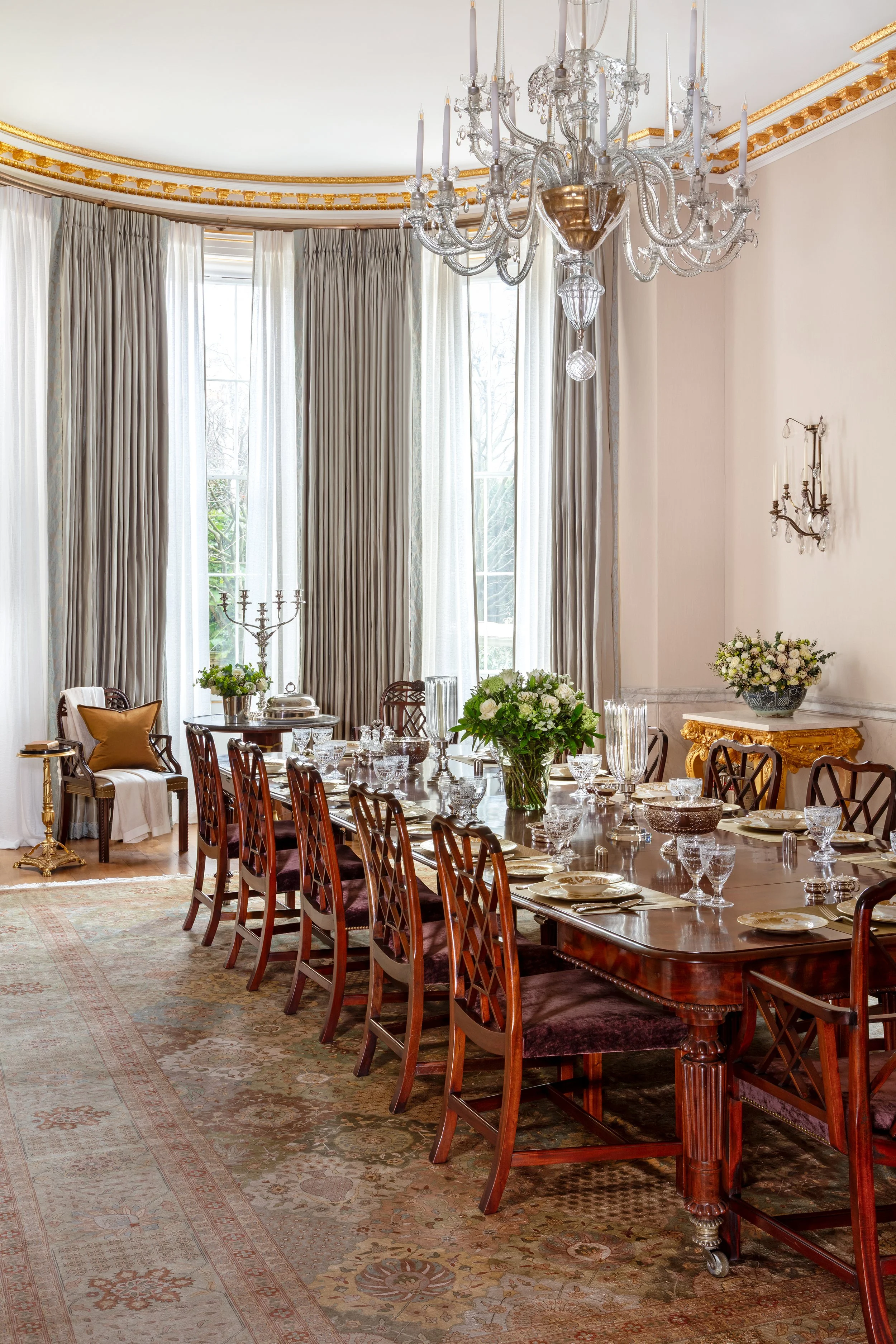 Grade I Listed Belgravia dining room with 18th-century antique table, antique rug, bespoke Dedar silk curtains, De Le Cuona sheers, Holland & Sherry wool fabric walls, and gilded detailing