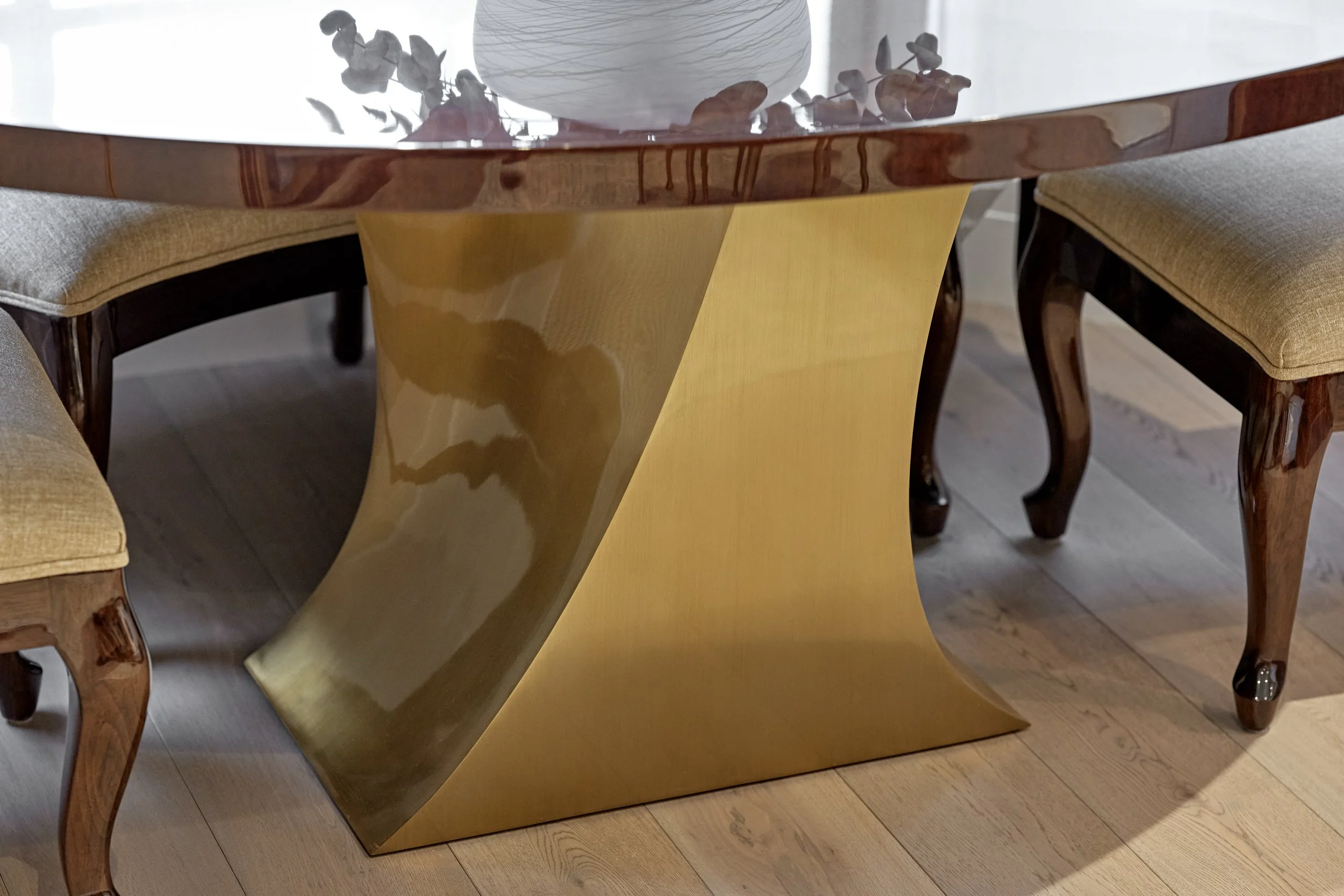 Round high-gloss dining table on a curved brass base with a dried flower arrangement in a Hyde Park apartment.