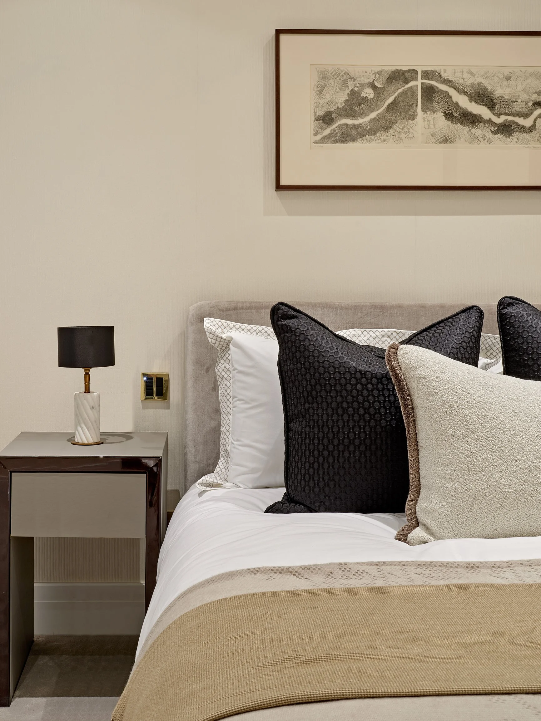 Bedroom with a grey velvet headboard, black and cream cushions and framed art in a Hyde Park apartment.