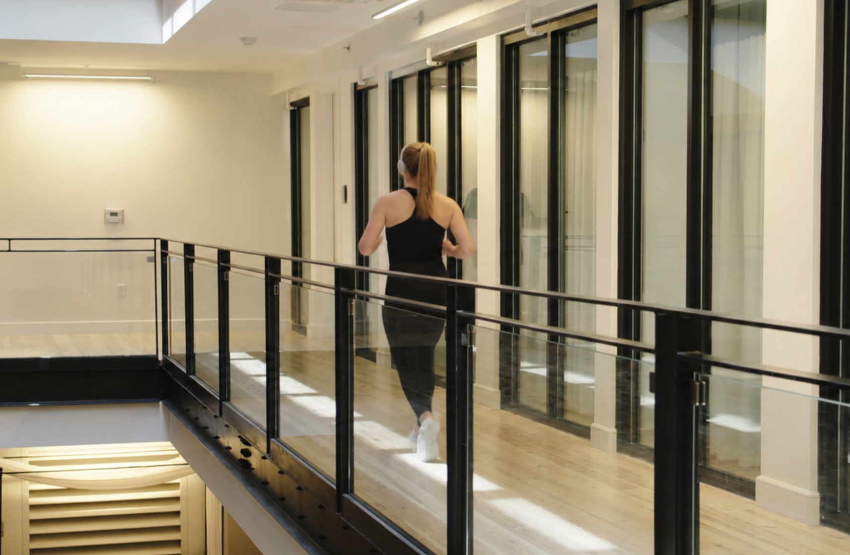 Woman wearing headphones and jogging through a bright indoor corridor during a convenient daily movement break.