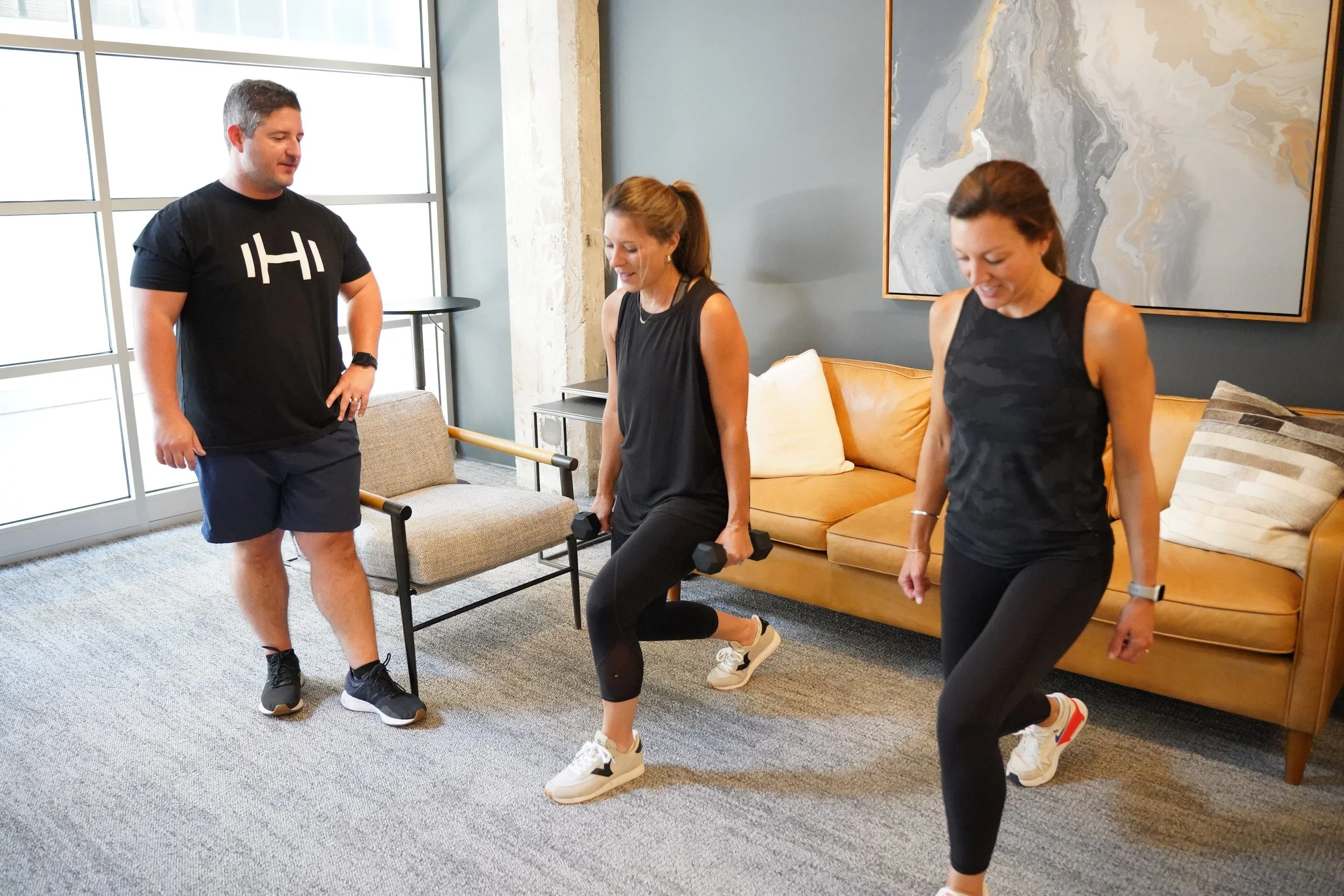 HOMEFIT personal trainer guiding two women through dumbbell lunges during an indoor small-group workout, highlighting in-home personal training, fitness accountability, and exercising with friends.