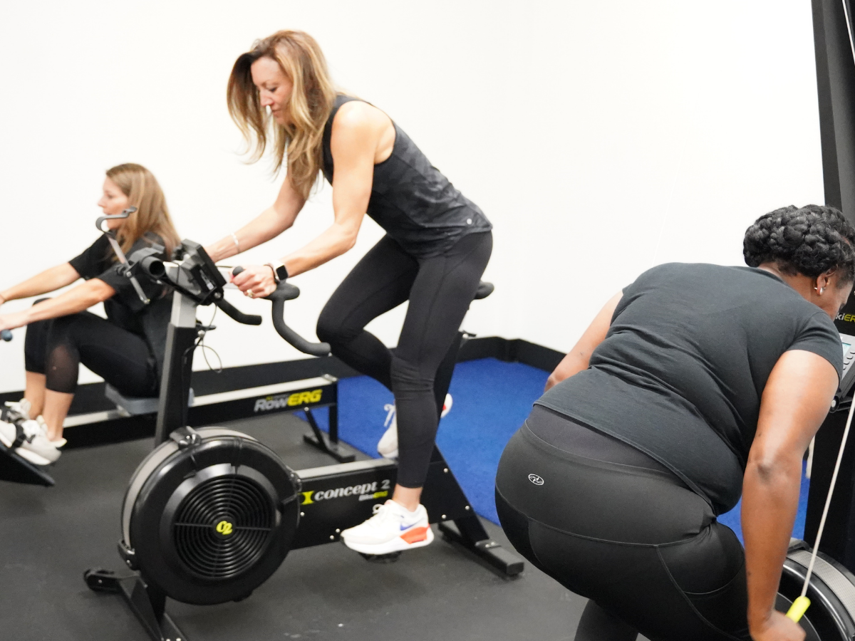 Women using indoor cardio equipment during a guided postnatal fitness workout focused on rebuilding endurance, core stability, and total-body strength.