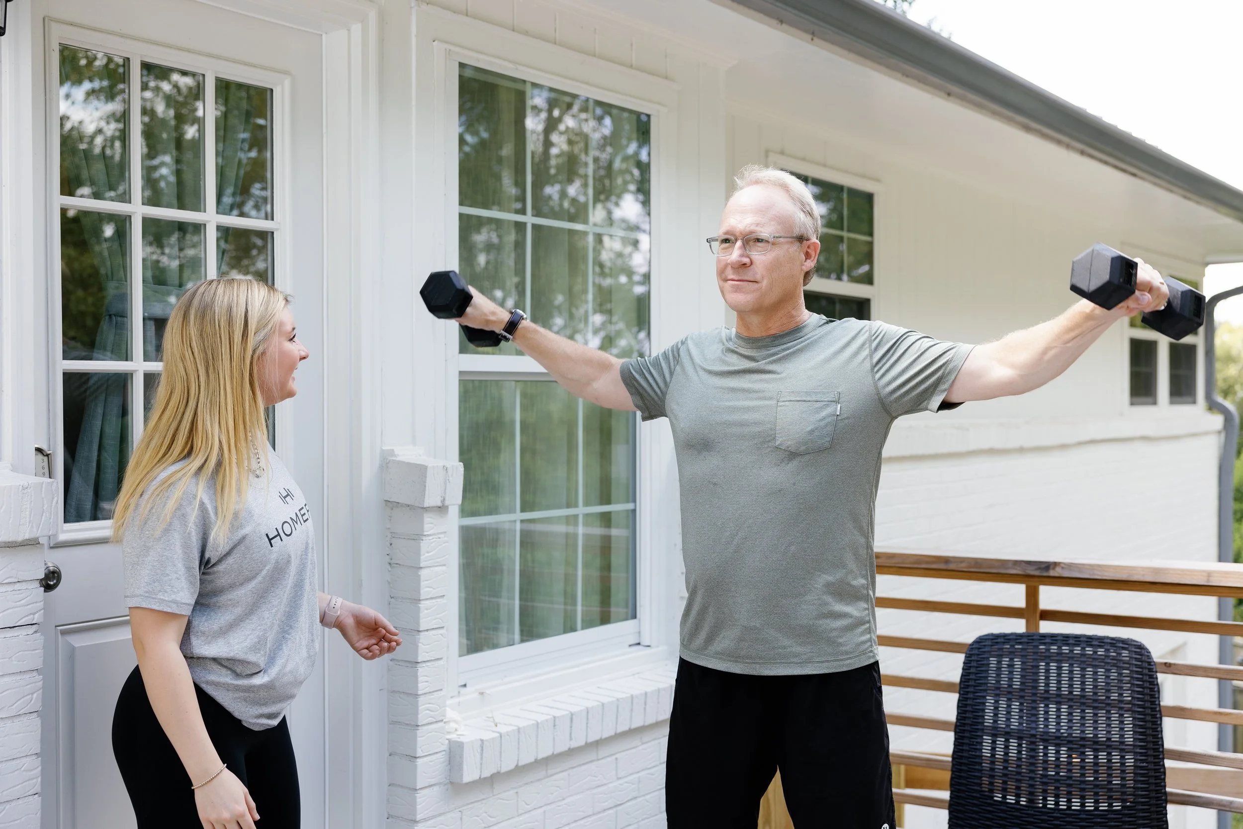 Older adult performing dumbbell shoulder raises with a HOMEFIT trainer during an in-home strength training workout.