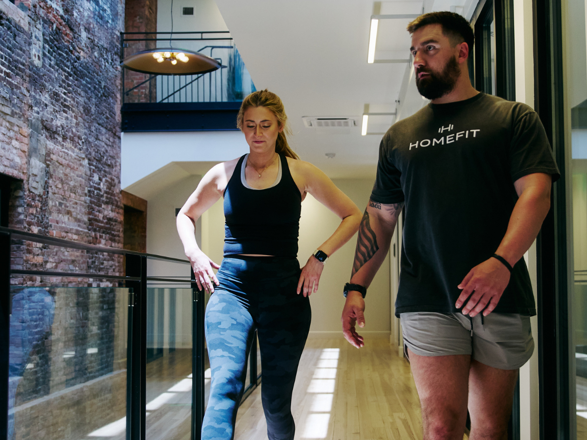 HOMEFIT personal trainer leading a client through a walking and movement assessment in a modern apartment building, emphasizing functional fitness, mobility, and personalized coaching.