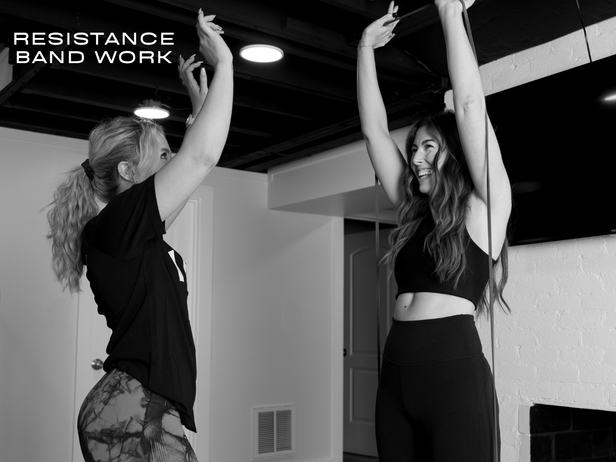 Personal trainer guides a client through gentle overhead resistance band work designed to support shoulder mobility and upper-body strength.