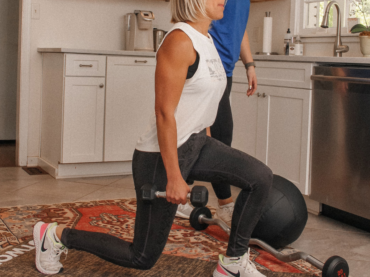 Postpartum client performing a supported reverse lunge with dumbbells during an in-home personal training session focused on rebuilding lower-body strength.