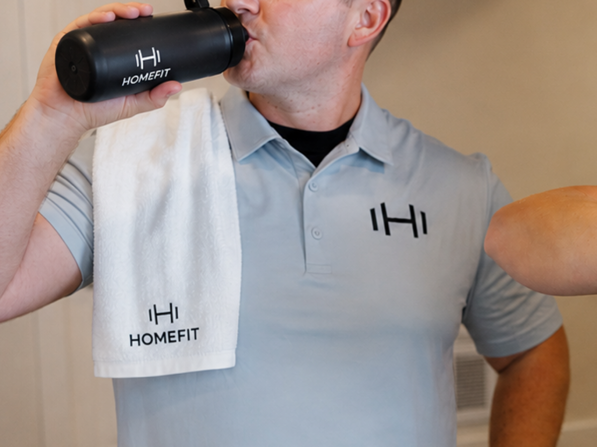 HOMEFIT trainer staying hydrated with a branded water bottle and towel after a workout.