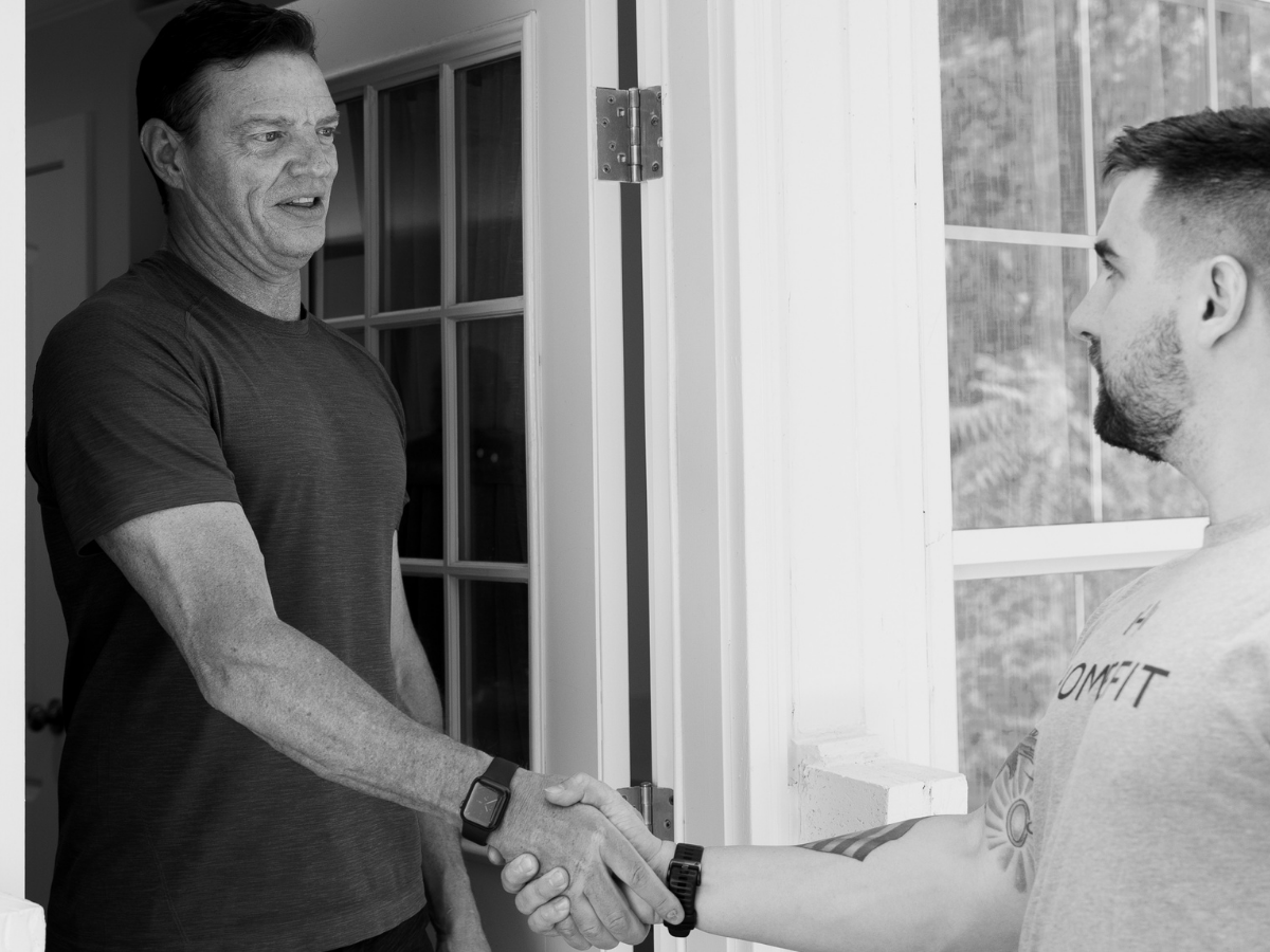 HOMEFIT trainer greeting a client at the door with a handshake, highlighting connection, support, and community during Mental Health Awareness Month.