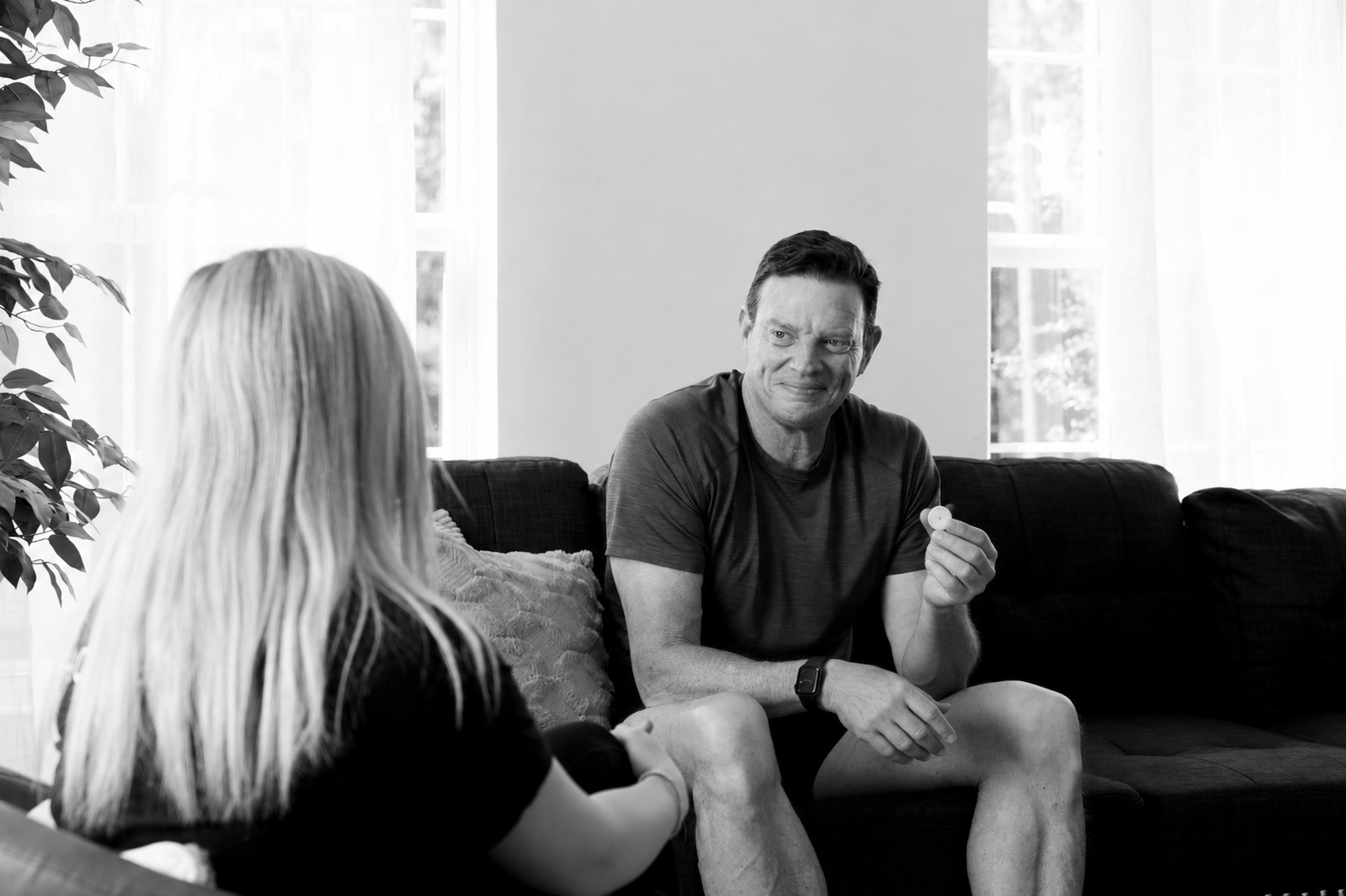 Man holding a continuous glucose monitor while discussing blood sugar and fitness goals with a HOMEFIT personal trainer at home.