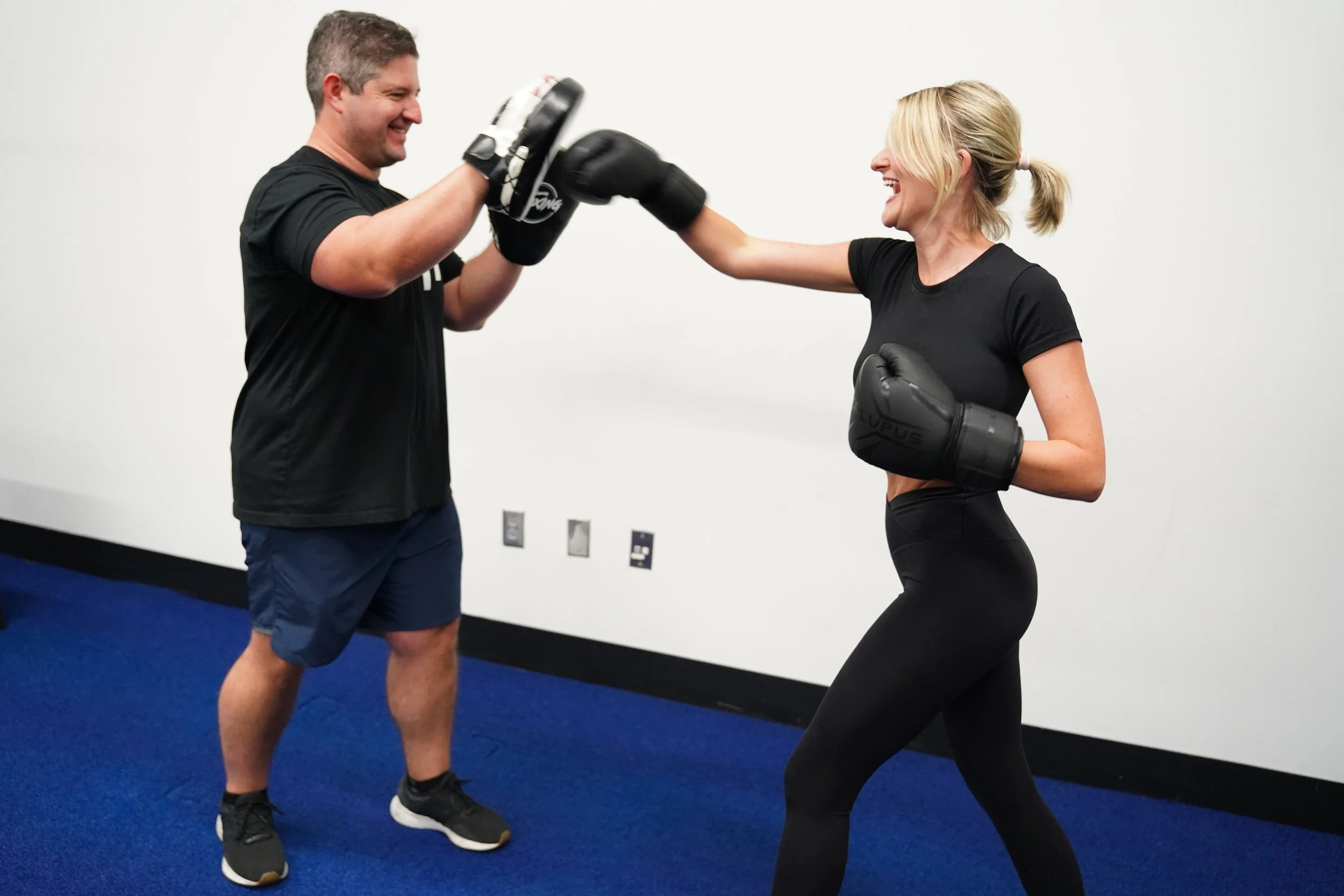 HOMEFIT personal trainer guiding a female client through boxing exercises with focus mitts, highlighting personalized strength training, fitness motivation, and sustainable workout routines for the 75 Soft Challenge.