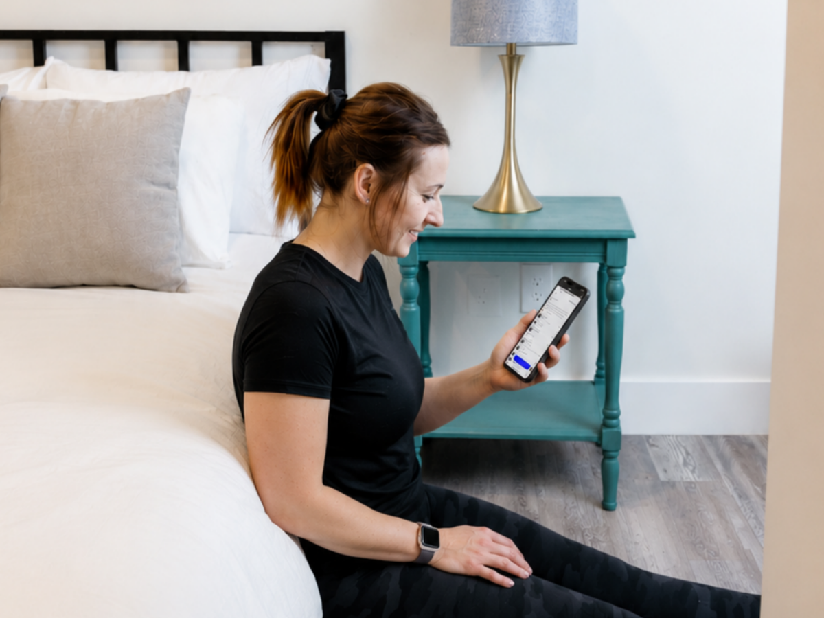 Woman using the HOMEFIT training app on her smartphone while exercising in a bedroom, showcasing the convenience of virtual personal training from home.
