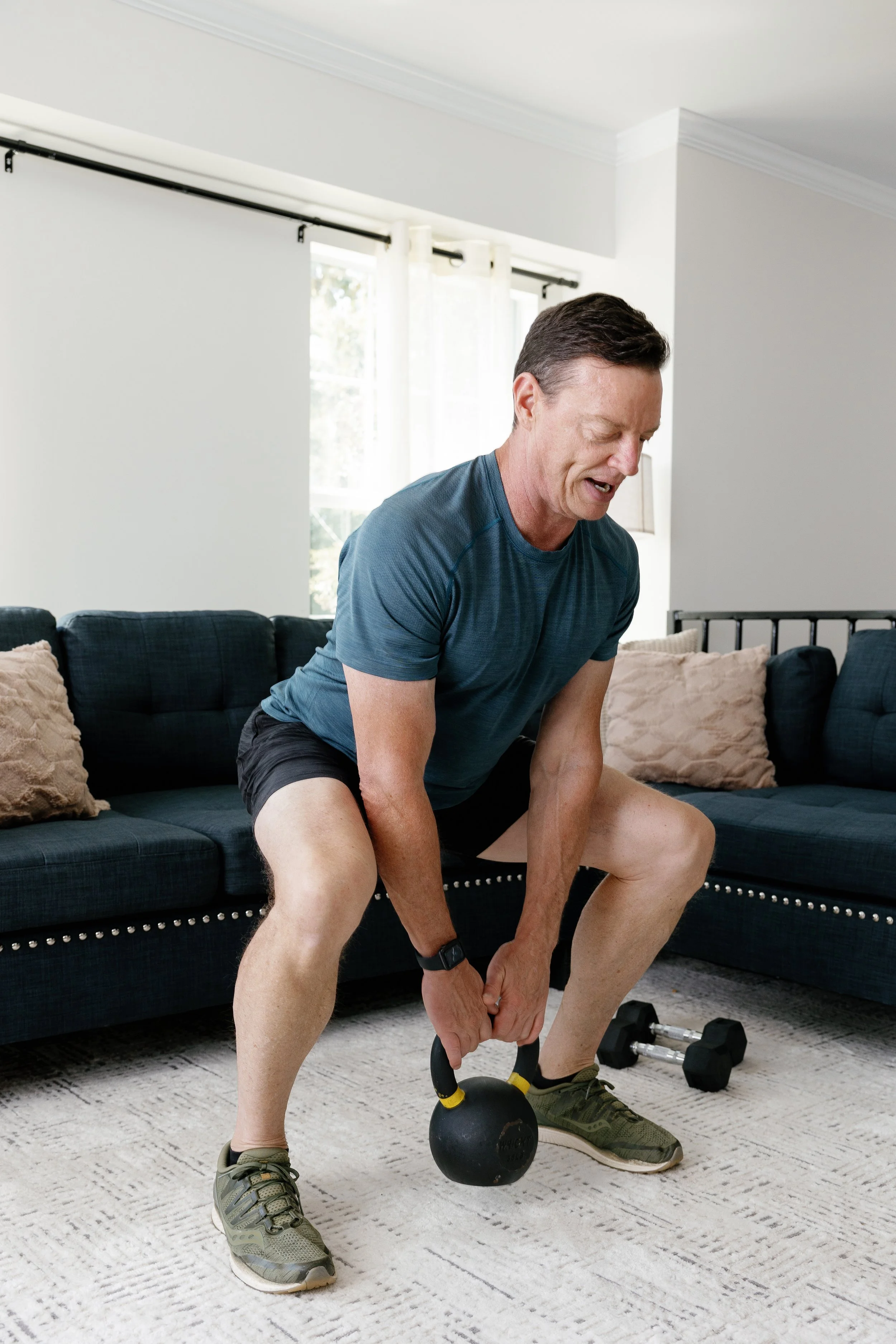 Client performing a kettlebell squat exercise in a living room during a customized HOMEFIT personal training workout.