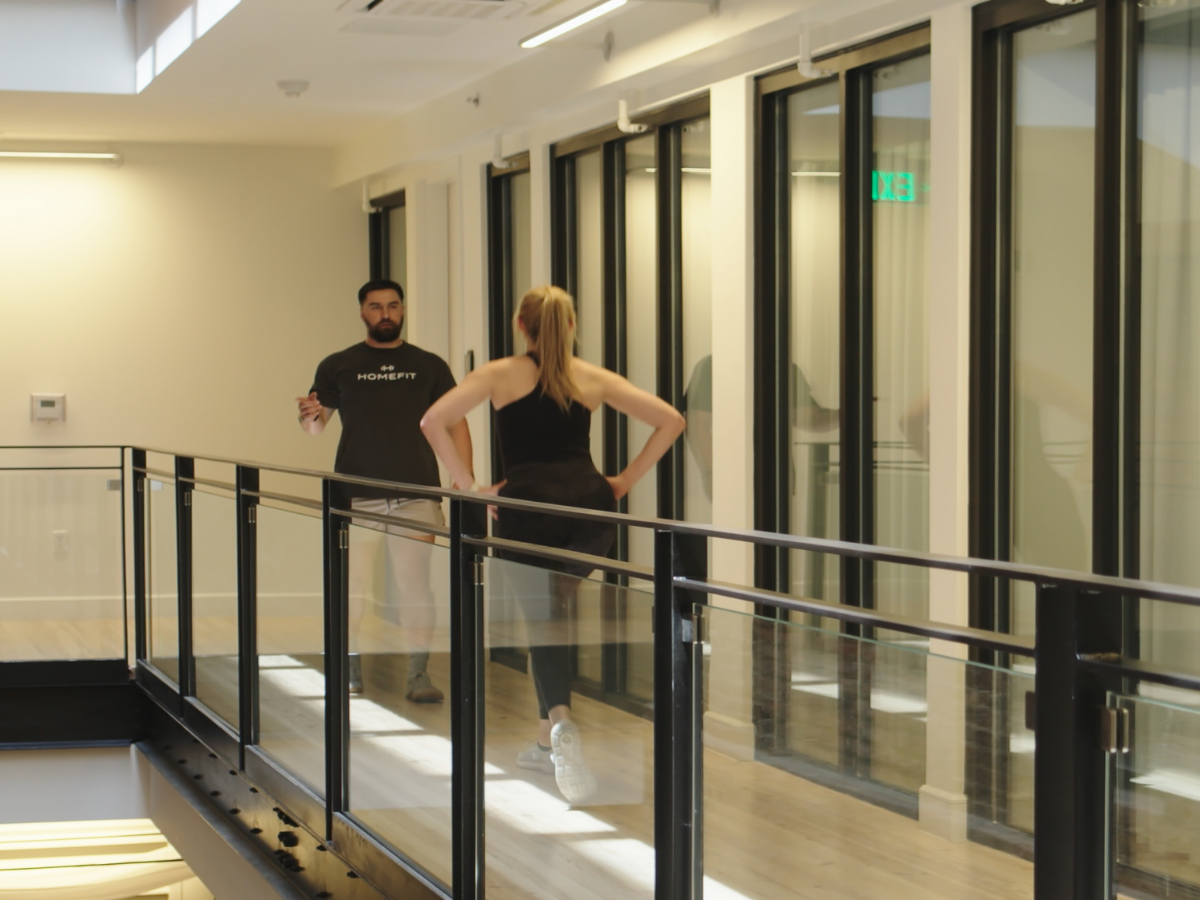 HOMEFIT personal trainer coaching a client during a cardio workout in a modern apartment building hallway, demonstrating convenient fitness training in residential spaces.