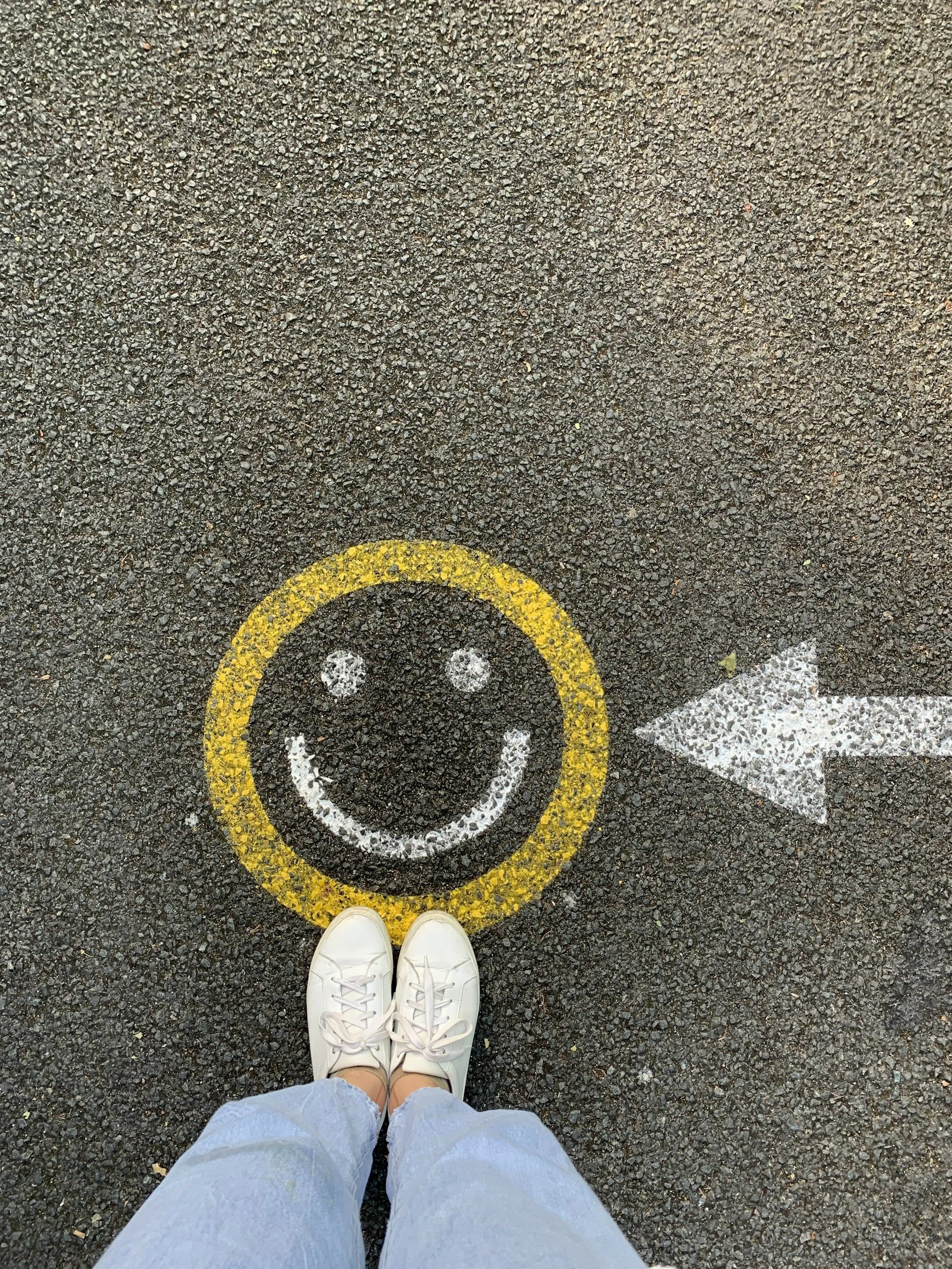 yellow smiley face on pavement with two white shoes nearby.