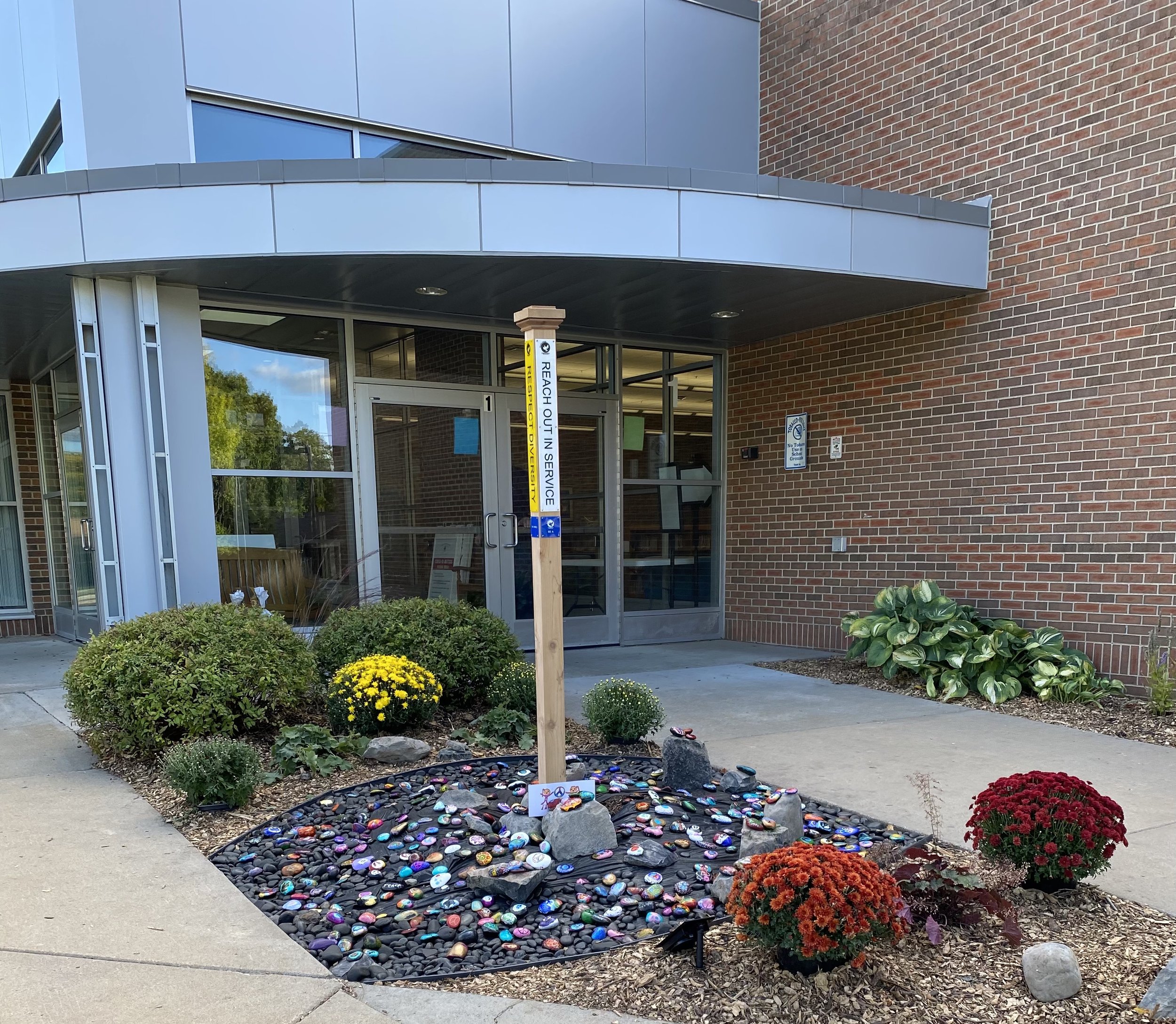 Peace pole and painted peace rock garden with a school in the background