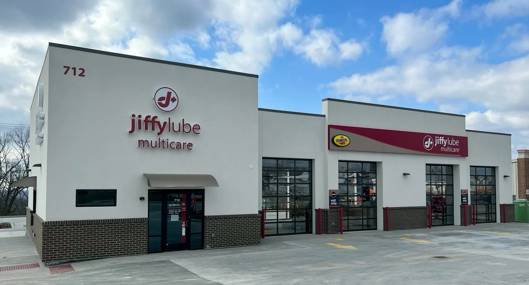 Exterior view of Jiffy Lube Multicare auto service center with Pennzoil logo, blue sky with clouds, and parking lot.