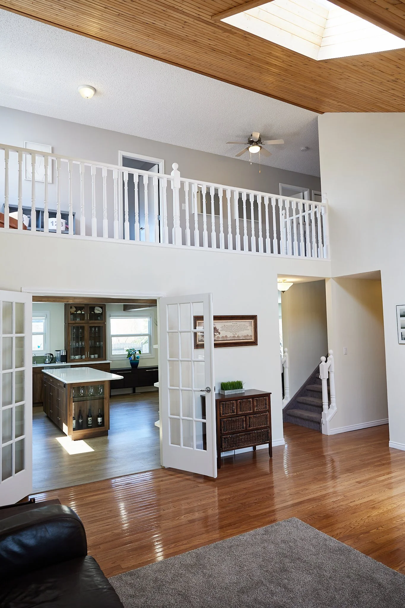 Interior view of a two-story home with hardwood floors, open space, a staircase, and French doors leading to a kitchen area.