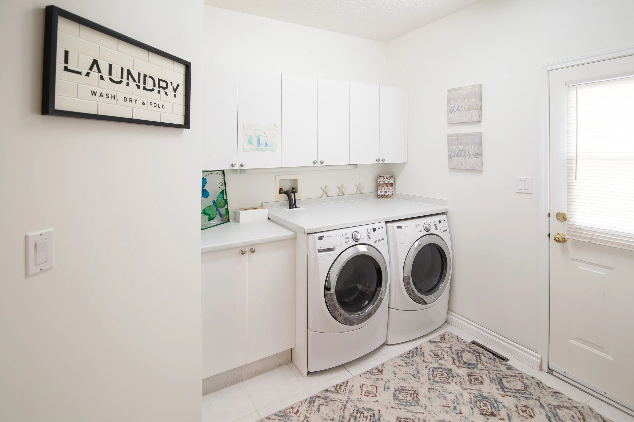 Laundry room with white cabinets, washer and dryer, decorative wall art, and a patterned rug.
