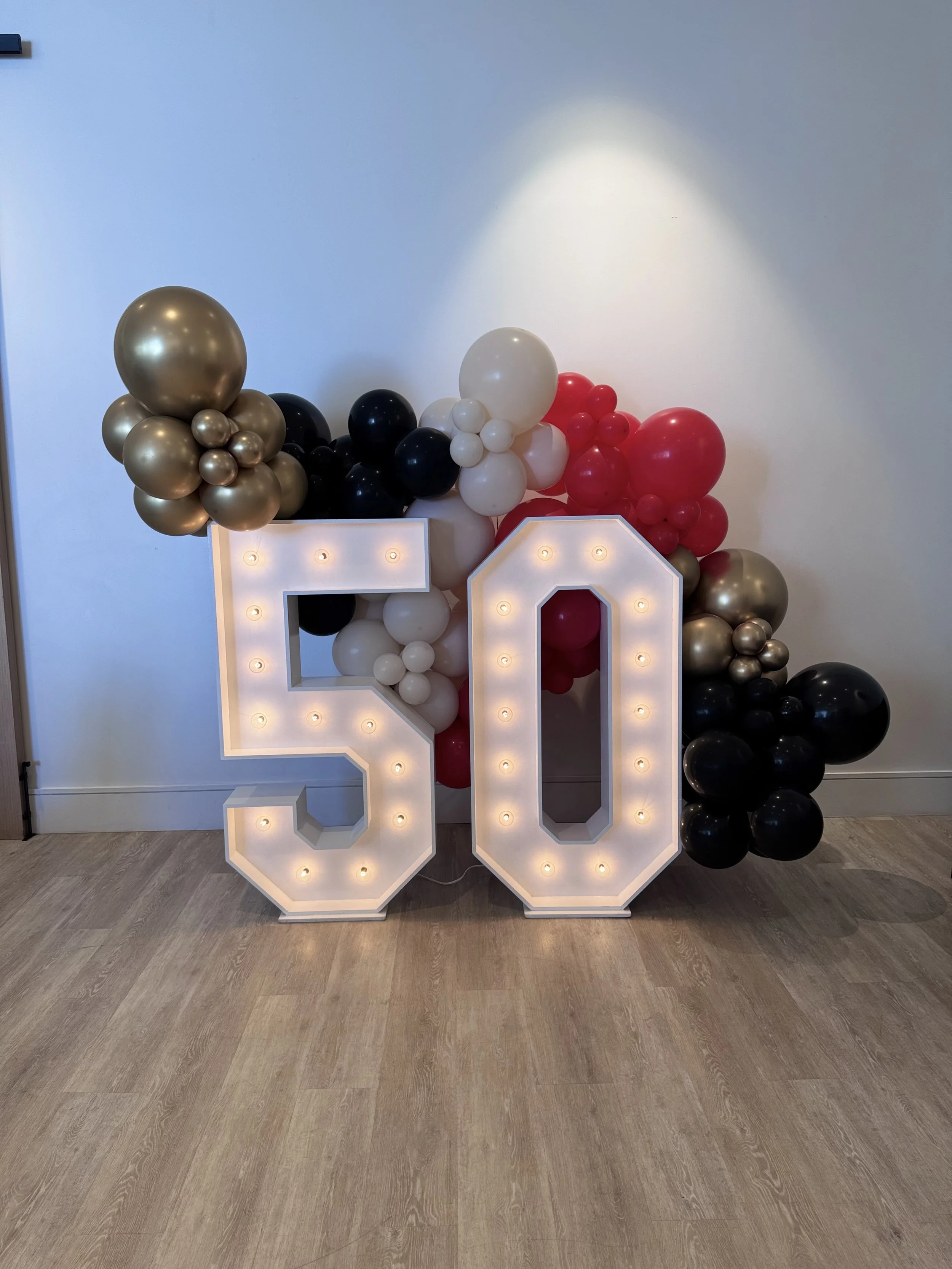 Illuminated marquee 50 with red, black, white and gold balloon garland for a corporate anniversary at VEA Newport Beach
