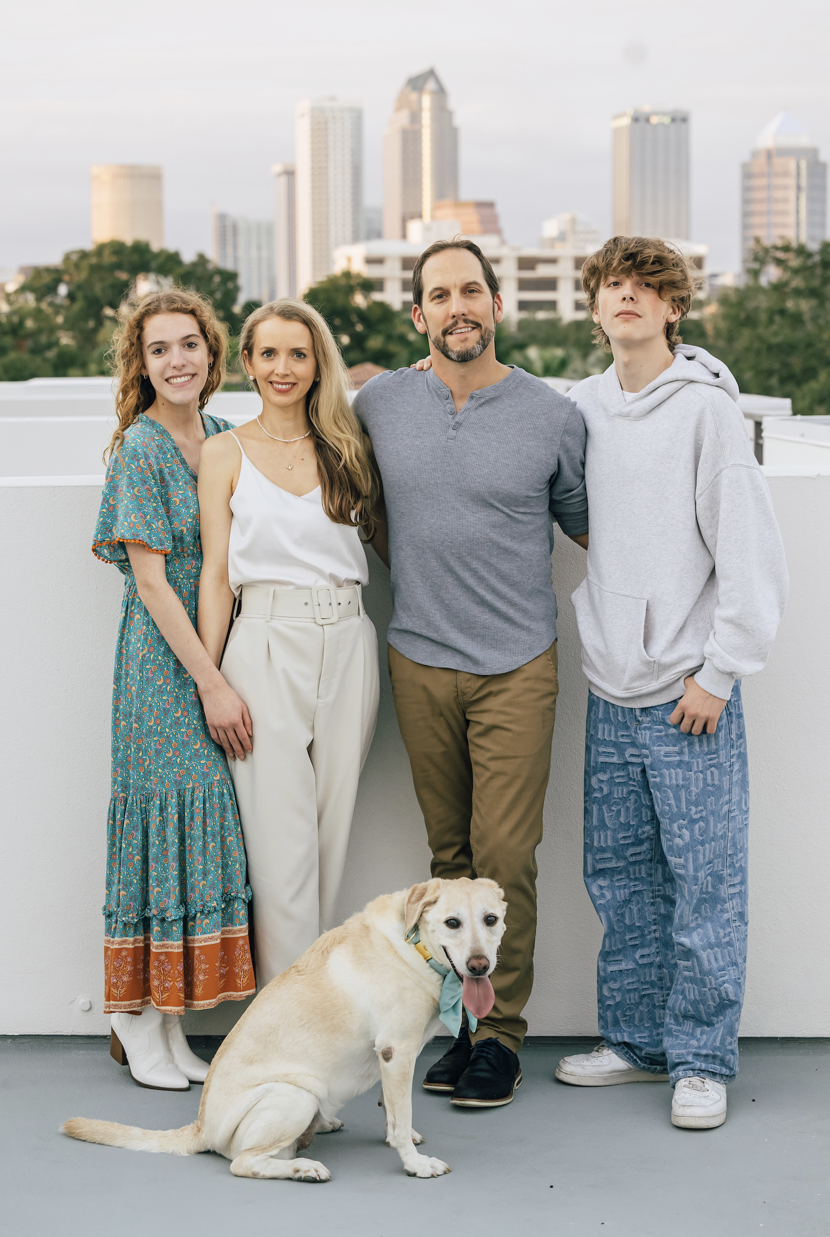 Family portrait on rooftop with cityscape background and a dog.