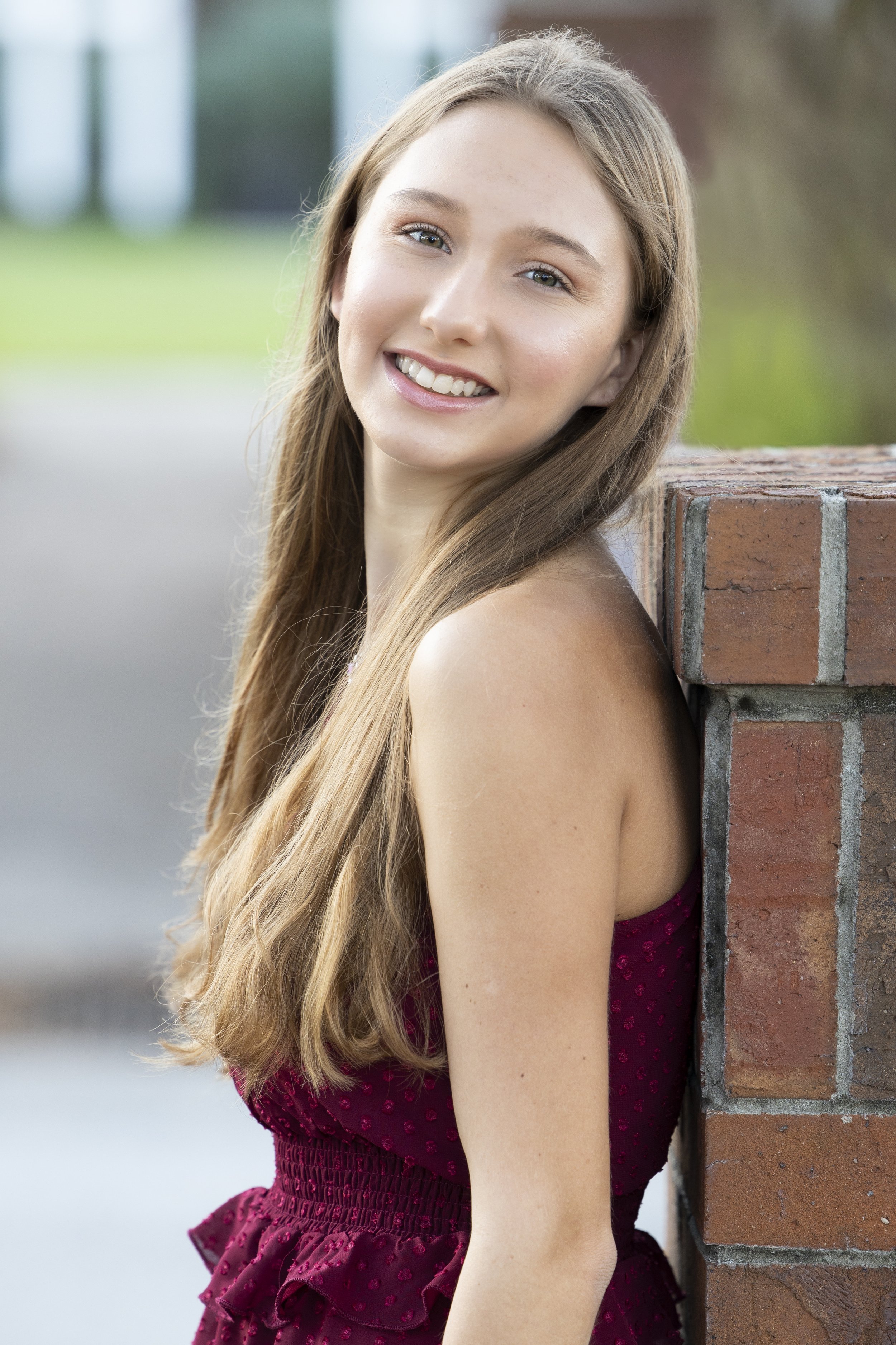 Woman in burgundy dress smiling near brick wall