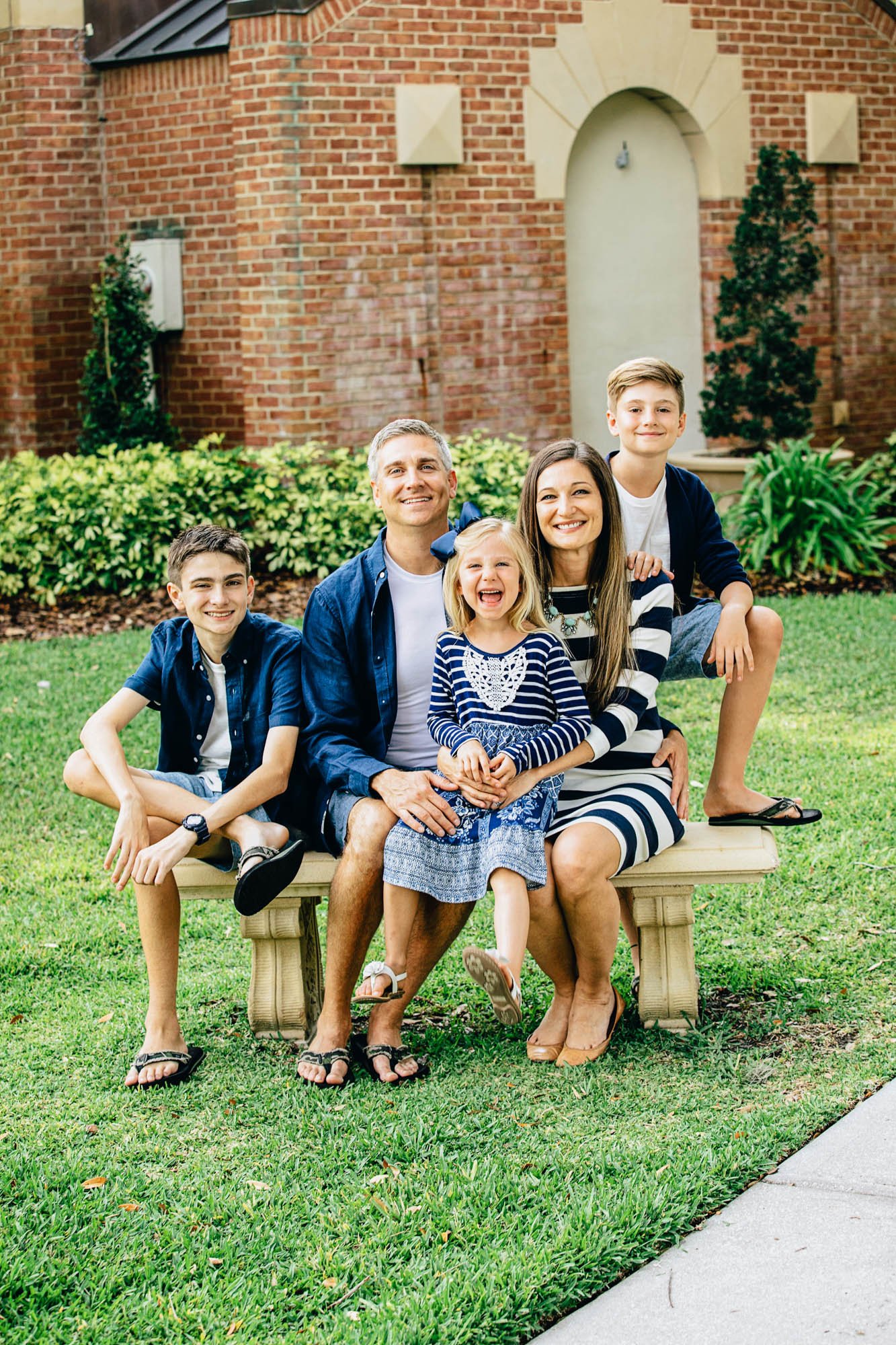 Family sitting on a bench in front of a brick building with greenery.